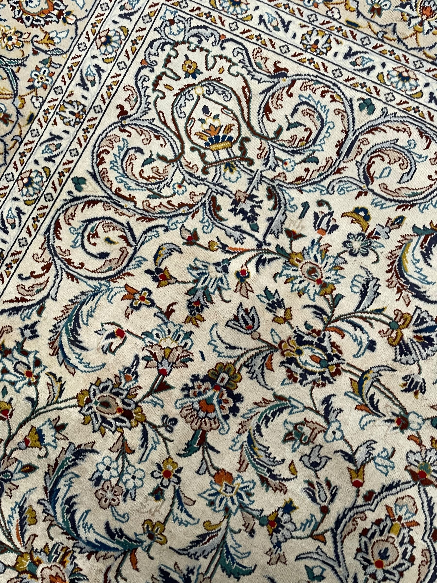 Persian Kashan ivory ground carpet, central pole medallion surrounded by swirling leafy branches and stylised plant motifs, scrolled foliate spandrels, the main border decorated with scrolling pattern and repeating palmettes, within floral patter guard stripes 