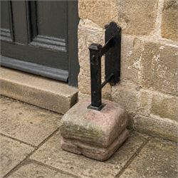 Large wrought metal boot scraper in black painted finish, set in formed stone plinth