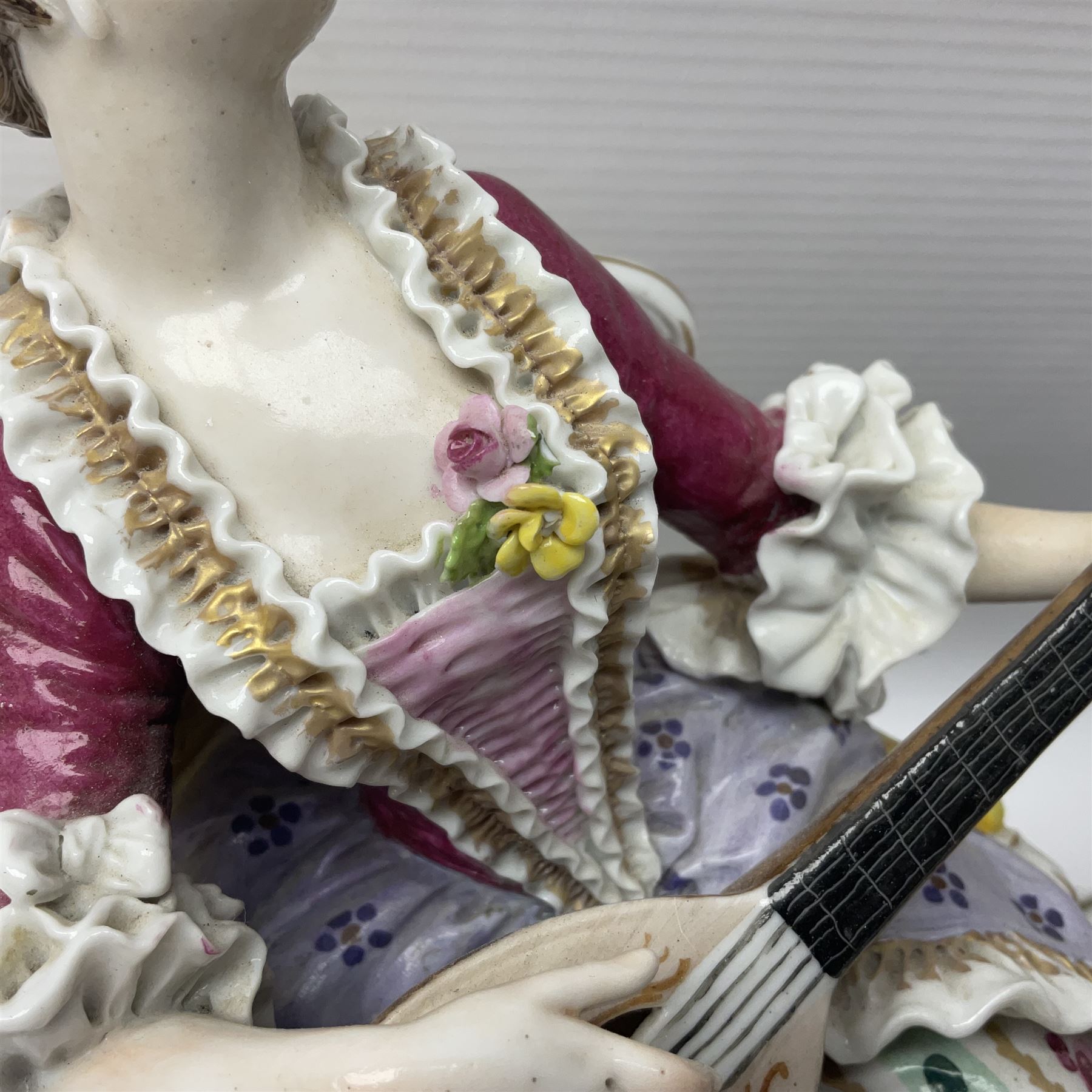 20th century Naples figure group, modelled as a seated female figure playing the lute seated, before a male figure stood holding a sheet of music, each in period dress, upon an oval base with gilt heightened scroll edge, with crowned N mark beneath, H31.5cm L33cm
