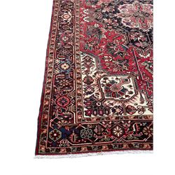 Persian Heriz red ground rug, central scrolled medallion on dark ground decorated with floral motifs, the surrounding field decorated with stylised plant motifs and smaller geometric symbols, guarded border with repeating pattern punctuated with rosettes and flower heads 