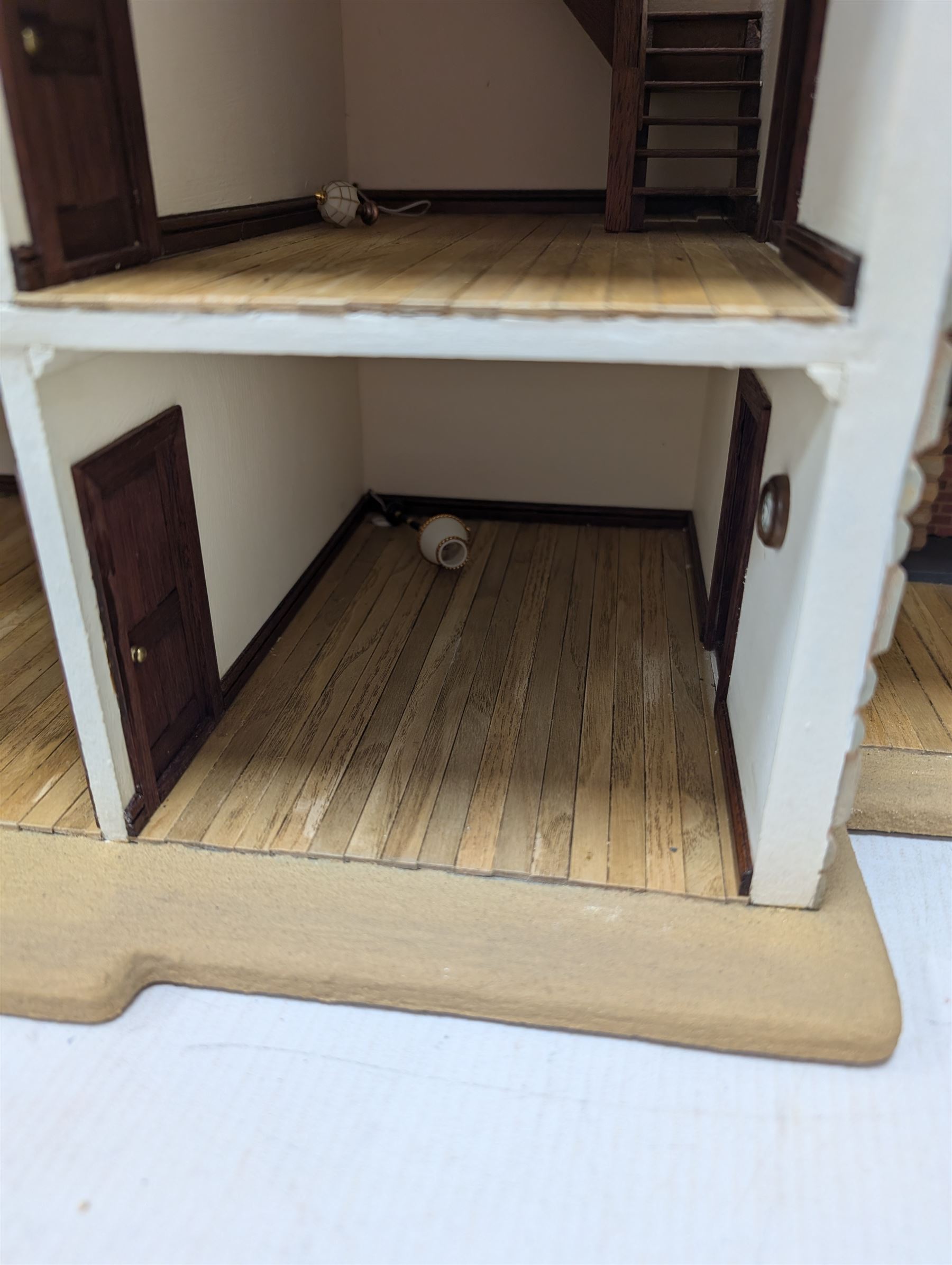 1:24 scale stone effect three-storey cottage dolls house, with green arched door and lattice effect windows, decorated to the interior with wooden floors, wired lighting and fire places, H45cm, W57cm, D26cm