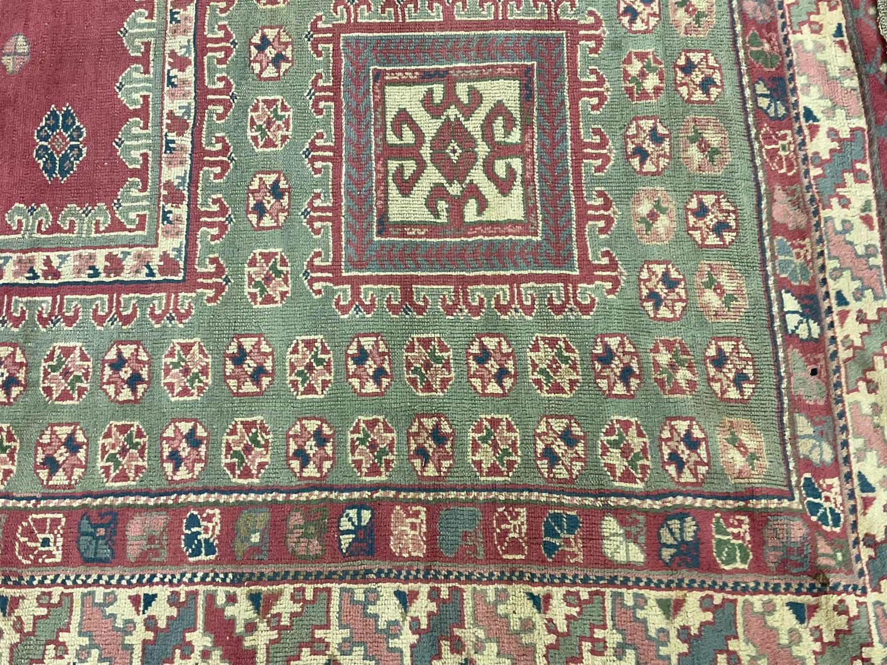 Turkish deep pink and green ground carpet, the square field with hooked borders surrounded by geometric motifs, multi-band border with overall geometric designs 