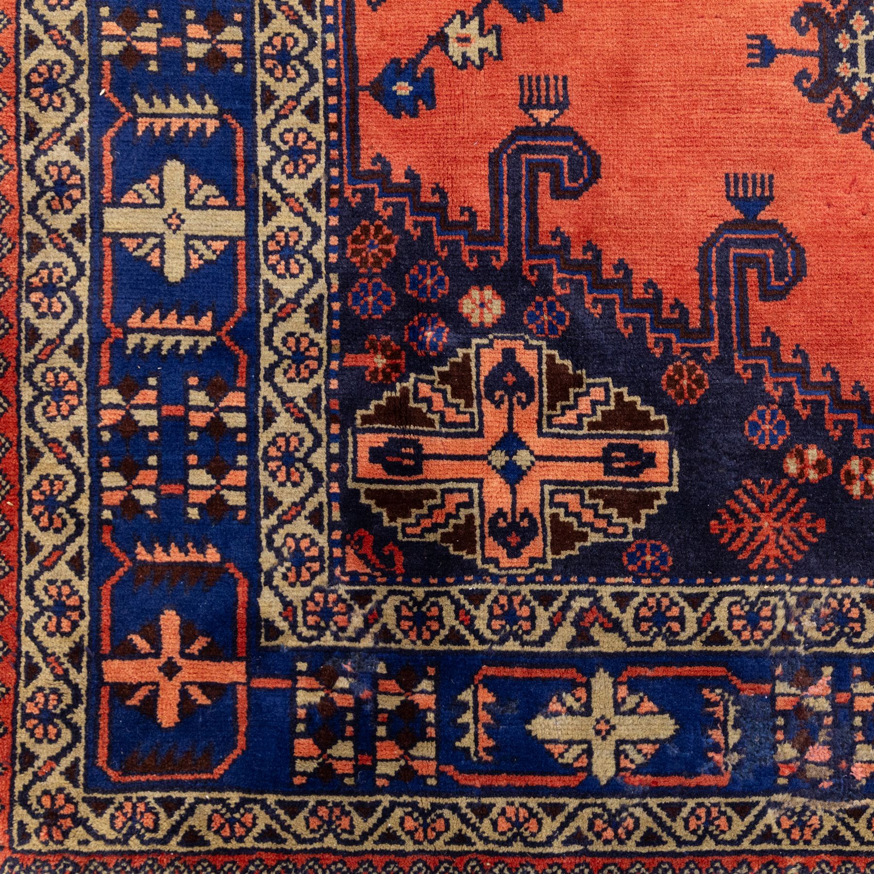 Central Persian Veis hand-knotted carpet, madder red field, decorated with a repeating arrangement of large octagonal and diamond medallions filled with stylized cross and geometric motifs and angular tribal devices within a series of geometric borders in tones of madder red, indigo blue, ivory, and soft green, with cotton fringe ends 