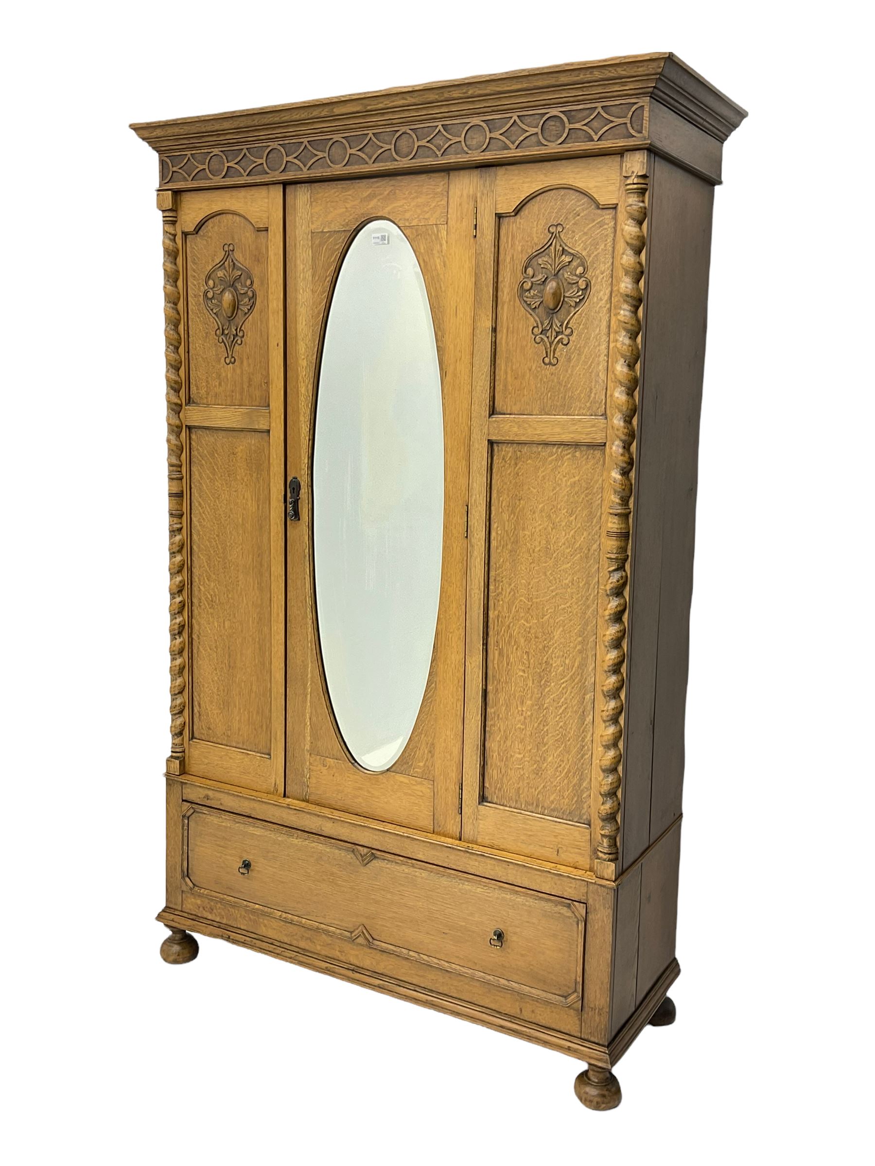 Early 20th century oak wardrobe, projecting cornice of blind fret-work frieze, oval bevel edge mirror door, half spiral turned pilasters, drawer to base with mouldings, on turned bun feet
