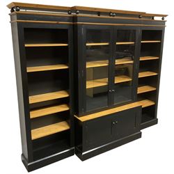 Contemporary polished pine and black finish break-front bookcase, projecting cornice over globular mounts, central cabinet enclosed by two glazed doors over double panelled cupboard, flanked by adjustable shelves, on plinth base
