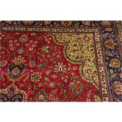 North East Persian Meshad hand-knotted carpet, crimson field with central lobed medallion in tones of indigo, ivory and soft blue, with an all-over arrangement of scrolling vinery, palmettes, and floral  sprays, conforming spandrels, main border of stylized floral vinery framed by multiple guard borders, with cotton fringe ends