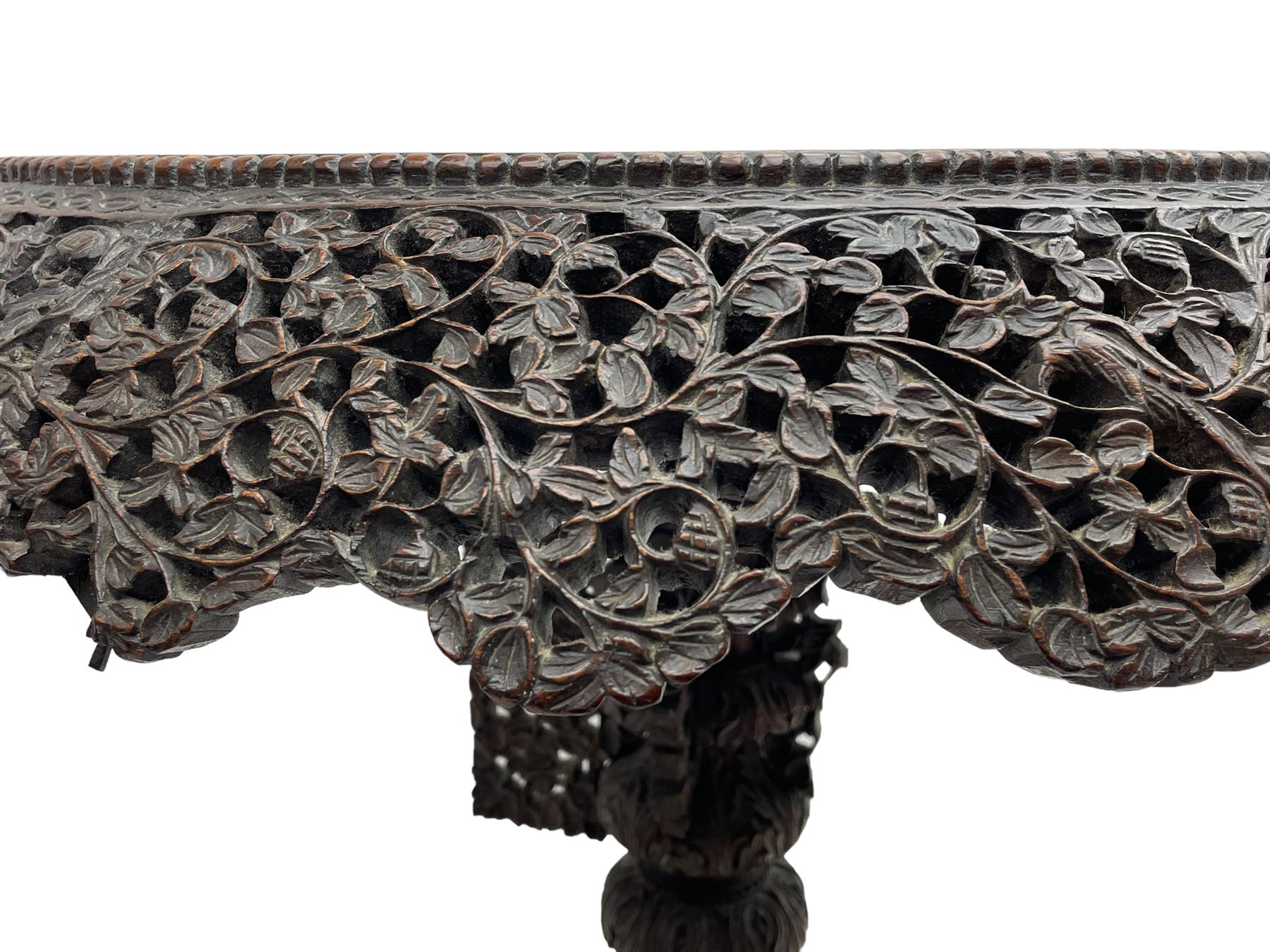 Late 19th century Anglo-Indian carved hardwood occasional table, circular tilt-top carved profusely with mythical animals and foliage decoration, pierced and carved with interlaced leafy branches, leaf carved pedestal supports on a raised platform with further carved and pierced foliage decoration, four carved feet in the form of mythical beasts with gaping jaws 