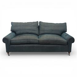 Late 20th century three seat sofa upholstered in green fabric, with gently rounded scroll arms, loose seat and back cushions, raised on turned wooden legs with castors, rear splayed legs