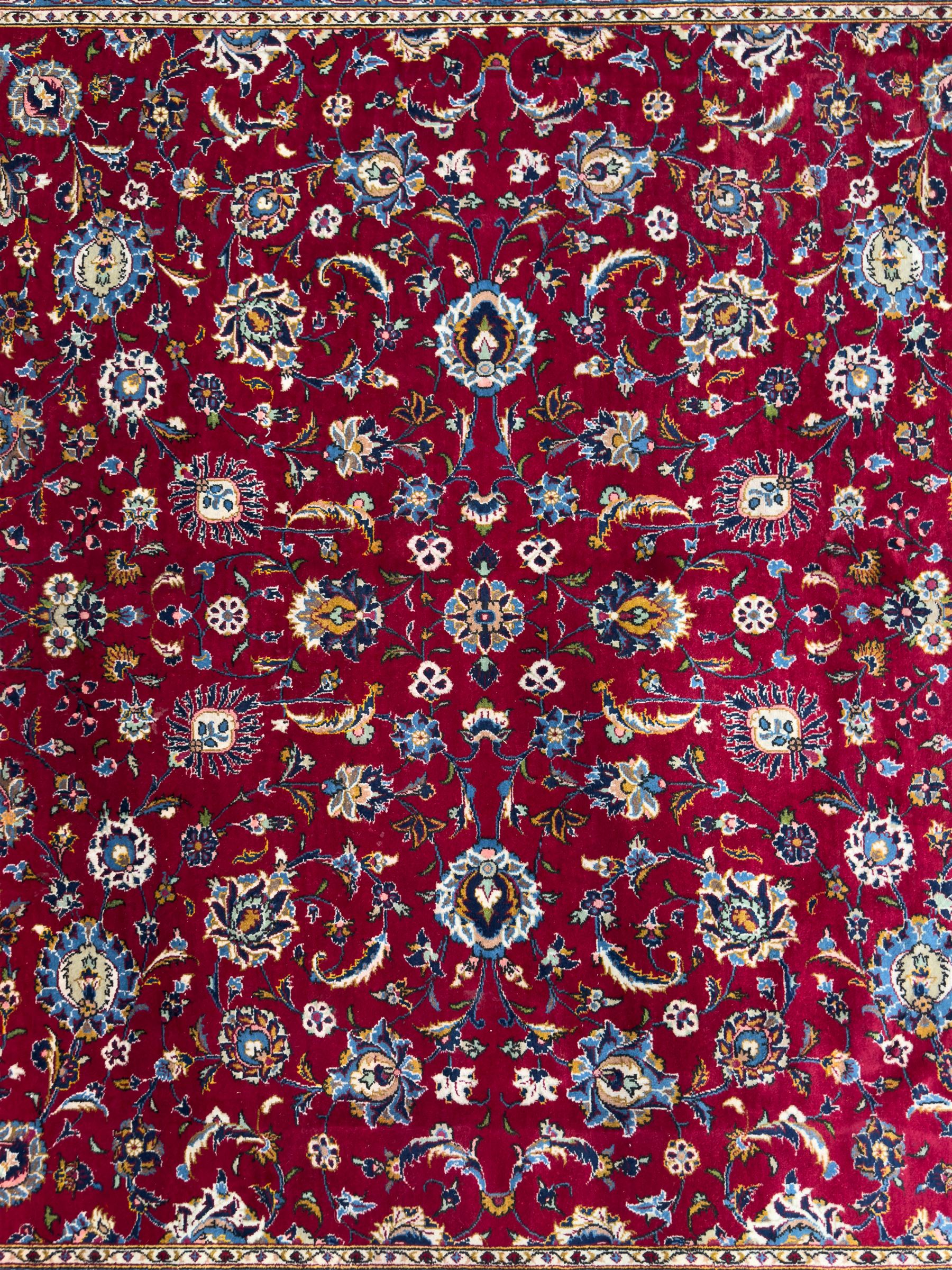 Northeastern Persian Meshed hand-knotted carpet, madder red field with an all-over design of scrolling vines, palmettes, and rosettes, within a dark blue border of palmettes and arabesques 