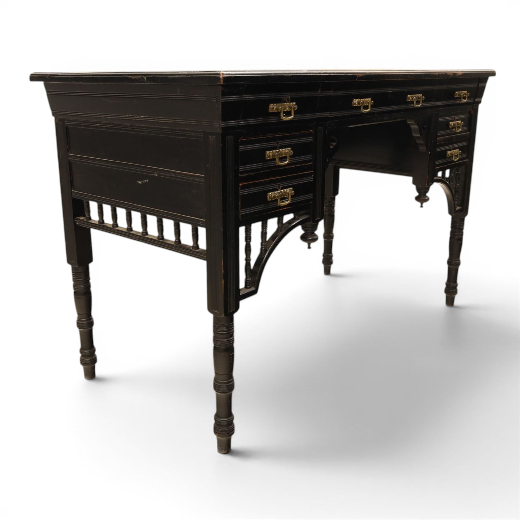Victorian Aesthetic Movement ebonised writing desk, rectangular top with inset tooled leather, central frieze drawer with pierced spandrels, flanked by two banks of three drawers, brass swing handles, raised on turned supports 