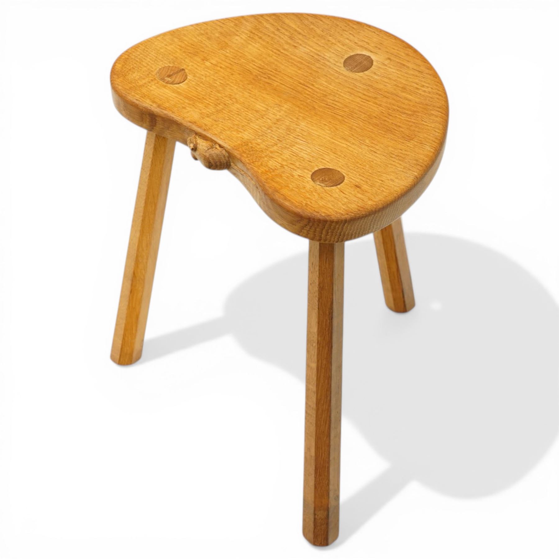 Mouseman - oak three-legged stool, dished kidney-shaped seat, raised on three octagonal splayed supports, with carved mouse signature, by the workshop of Robert Thompson of Kilburn