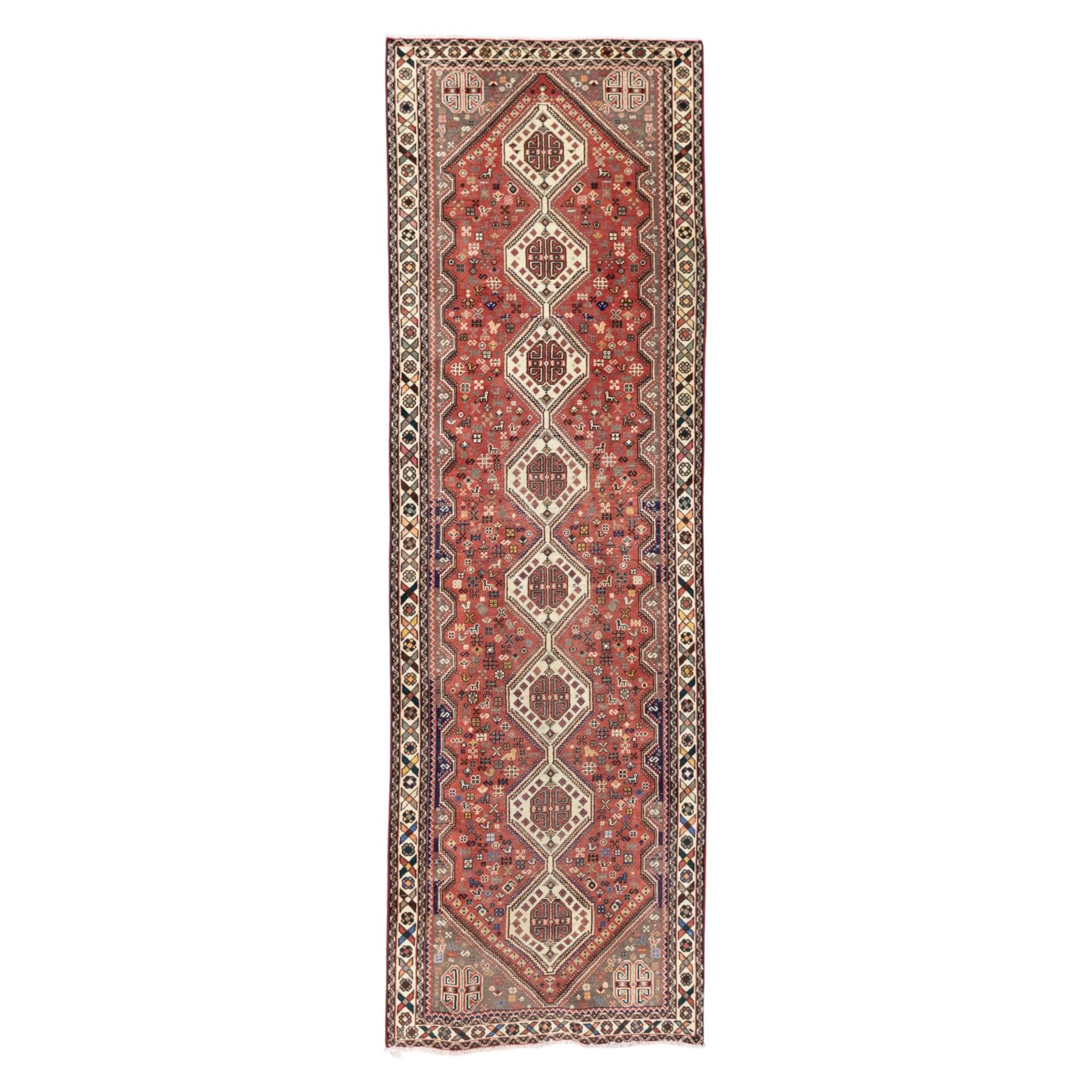 South West Persian Abadeh hand-knotted runner, madder red field decorated with a vertical sequence of stepped lozenge medallions, each enclosing stylized geometric motifs and angular devices, surrounding field filled with tribal symbols and abstract forms, enclosed within a narrow main border and flanked by multiple guard stripes, with fringe ends 
