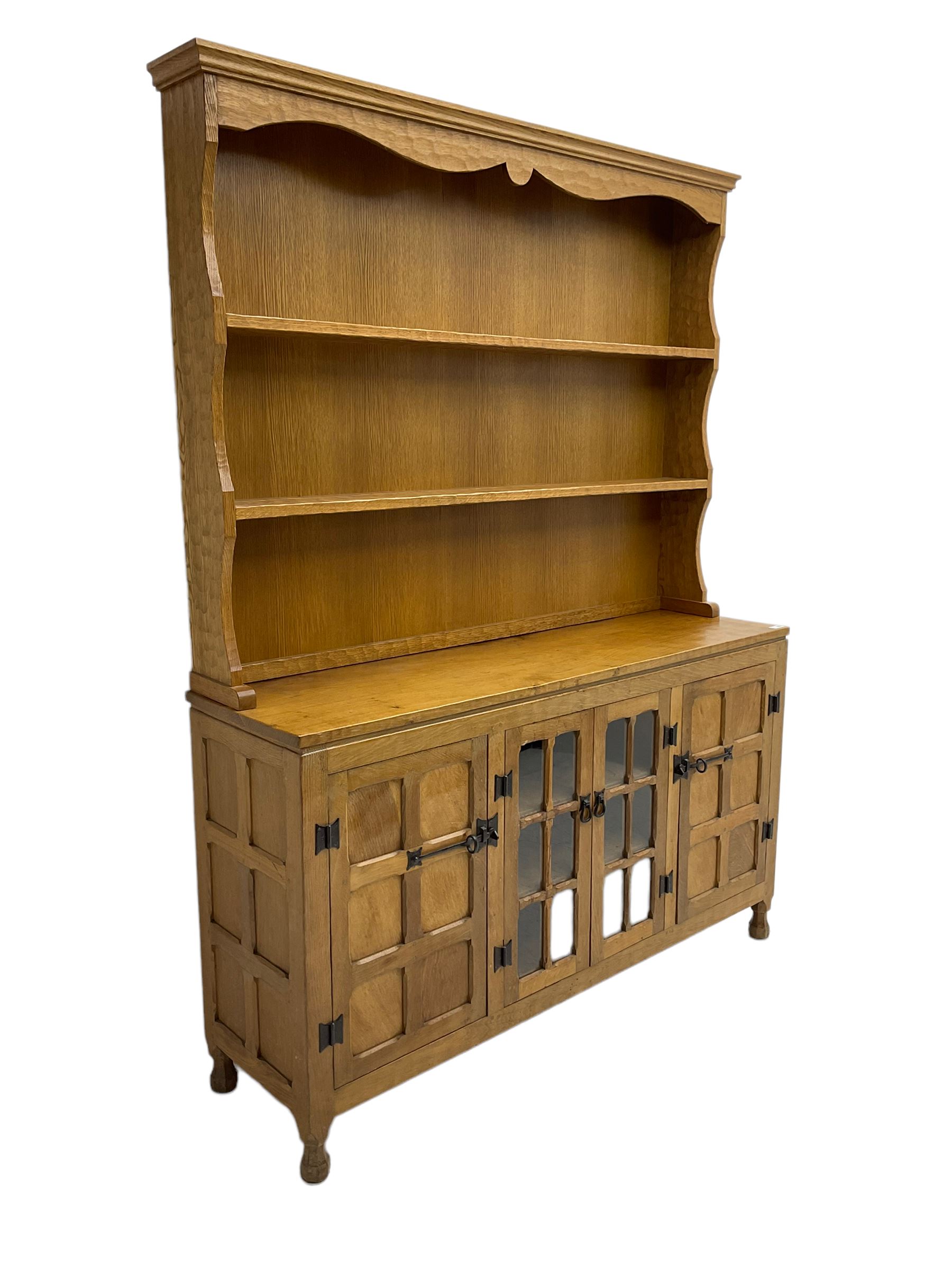 Yorkshire oak - adzed oak dresser, the rack with projecting cornice over shaped frieze and two shelves, the dresser fitted with central glazed double cupboard flanked by two panelled single cupboards, panelled sides