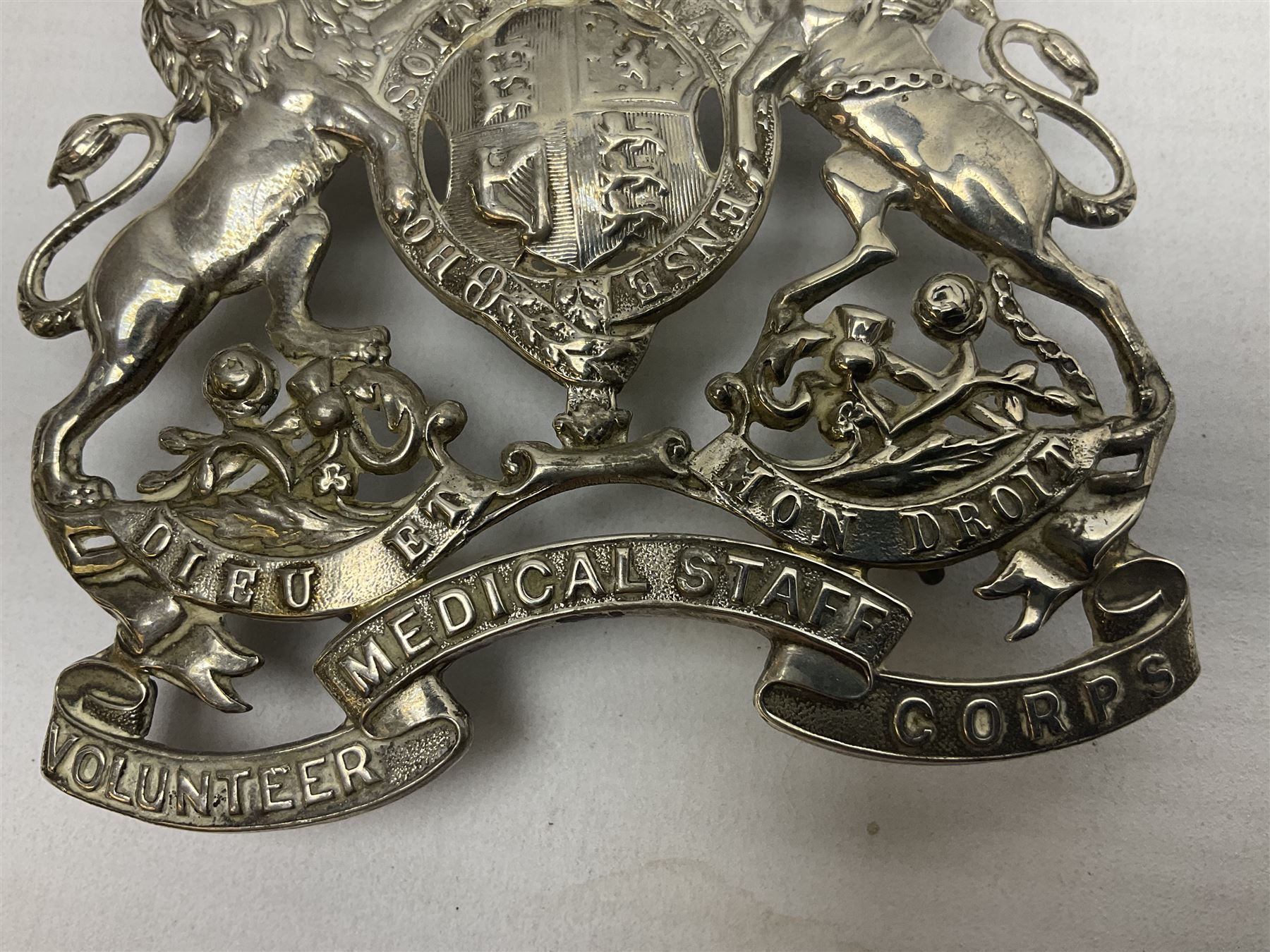 Victorian Volunteer Medical Staff Corps white metal helmet plate in the form of Victorian crowned Royal Arms with three part lower scroll for “VOLUNTEER MEDICAL STAFF CORPS”; three lug fittings to the reverse L8.5cm