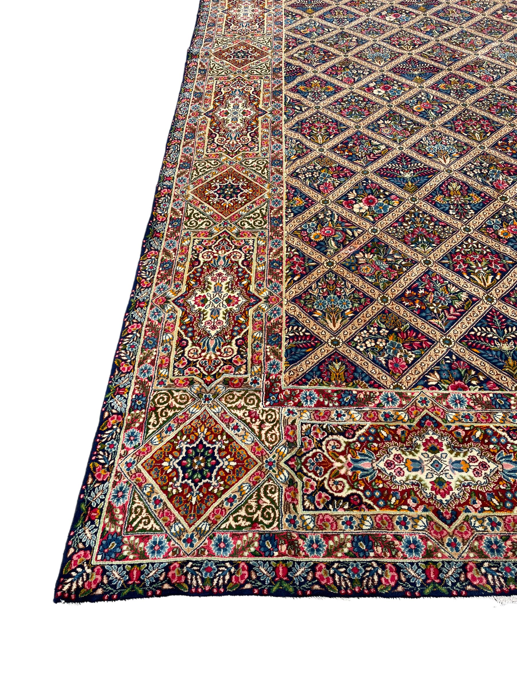 Persian Kirman indigo ground carpet, the field with repeating lozenge tiles with overall floral decoration, the main border with floral panels enclosed by the guards