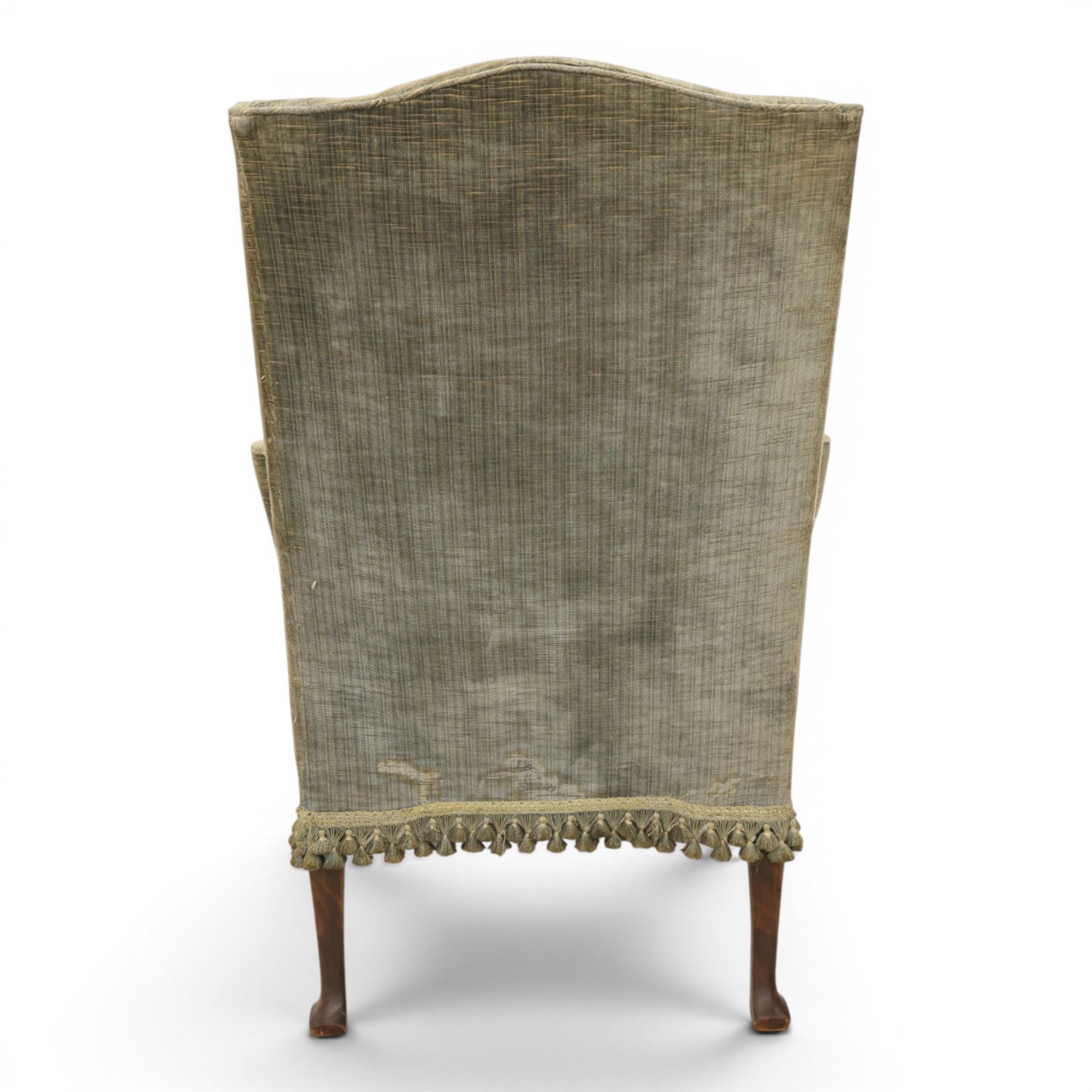 Pair of Georgian style wing armchairs, upholstered in green velvet, each with shaped wing backs, padded scroll arms and loose seat cushions, raised on cabriole supports terminating in pad feet, one with tasselled fringe