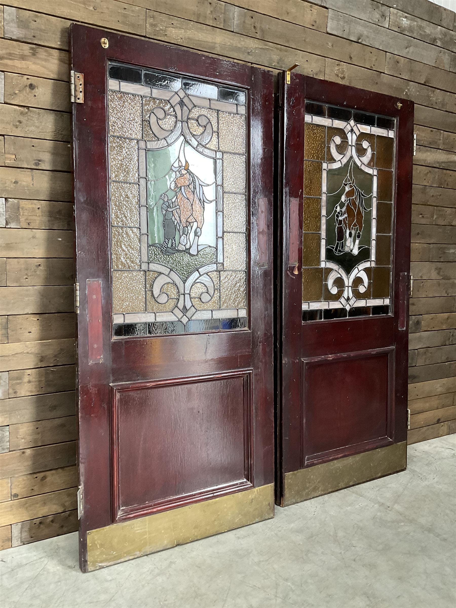 Two early to mid 20th century timber doors, set with lead framed stained glass panels depicting agricultural worker and horse