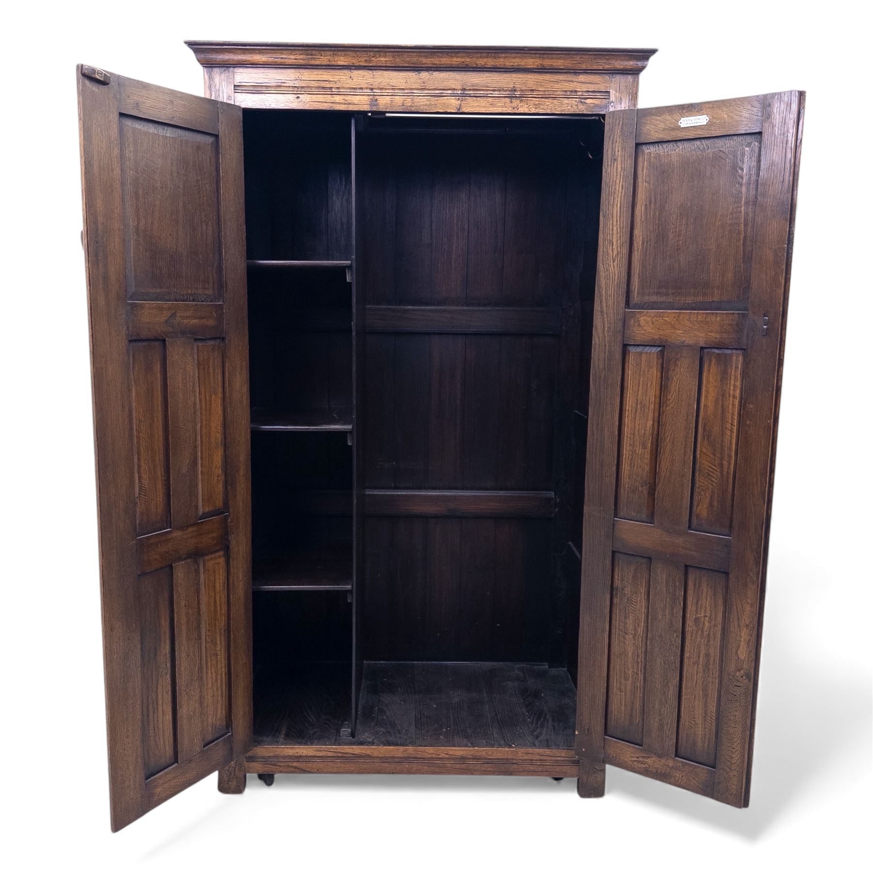Mid 20th century oak double wardrobe, the rectangular top above twin panelled doors with carved linenfold decoration and wrought iron hinges, raised on block feet