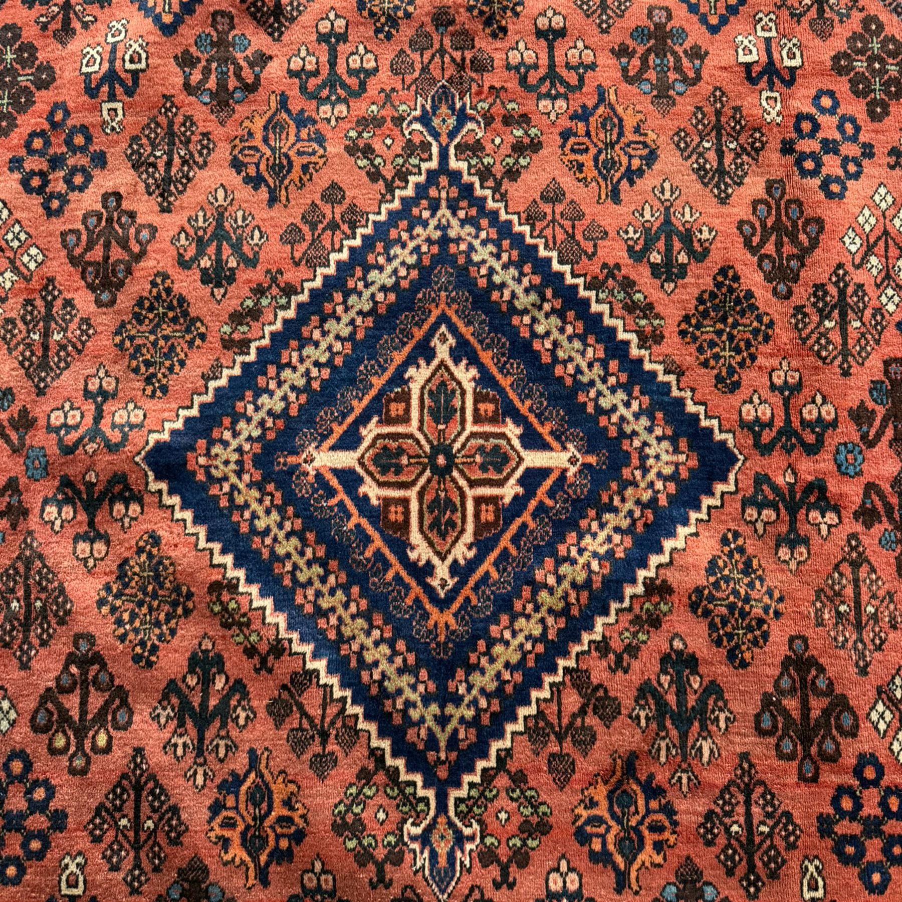 Joshgan Persian wool rug, with diamond-framed medallion, on a deep red field filled with geometric-shaped floral motifs and indigo-filled spandrels 