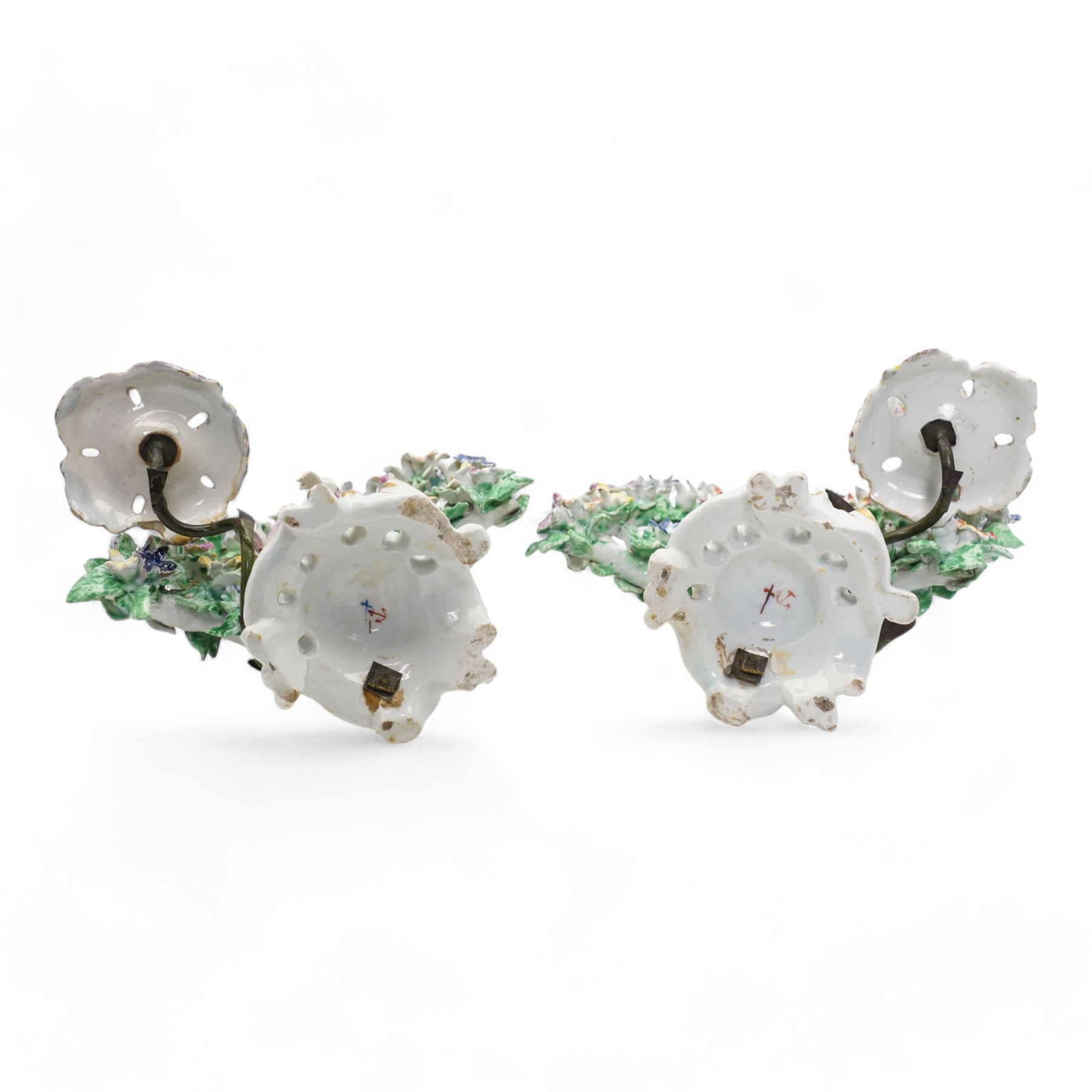 Pair of Bow porcelain 'New Dancers' candlesticks, standing before flowering bocages, and wearing brightly coloured flowered clothes, each supporting to left and right a tôle peinte branch terminating in a leaf moulded nozzle, on scrolling footed bases, red anchor and blue/red dagger marks beneath, H19cm x W18cm (2)