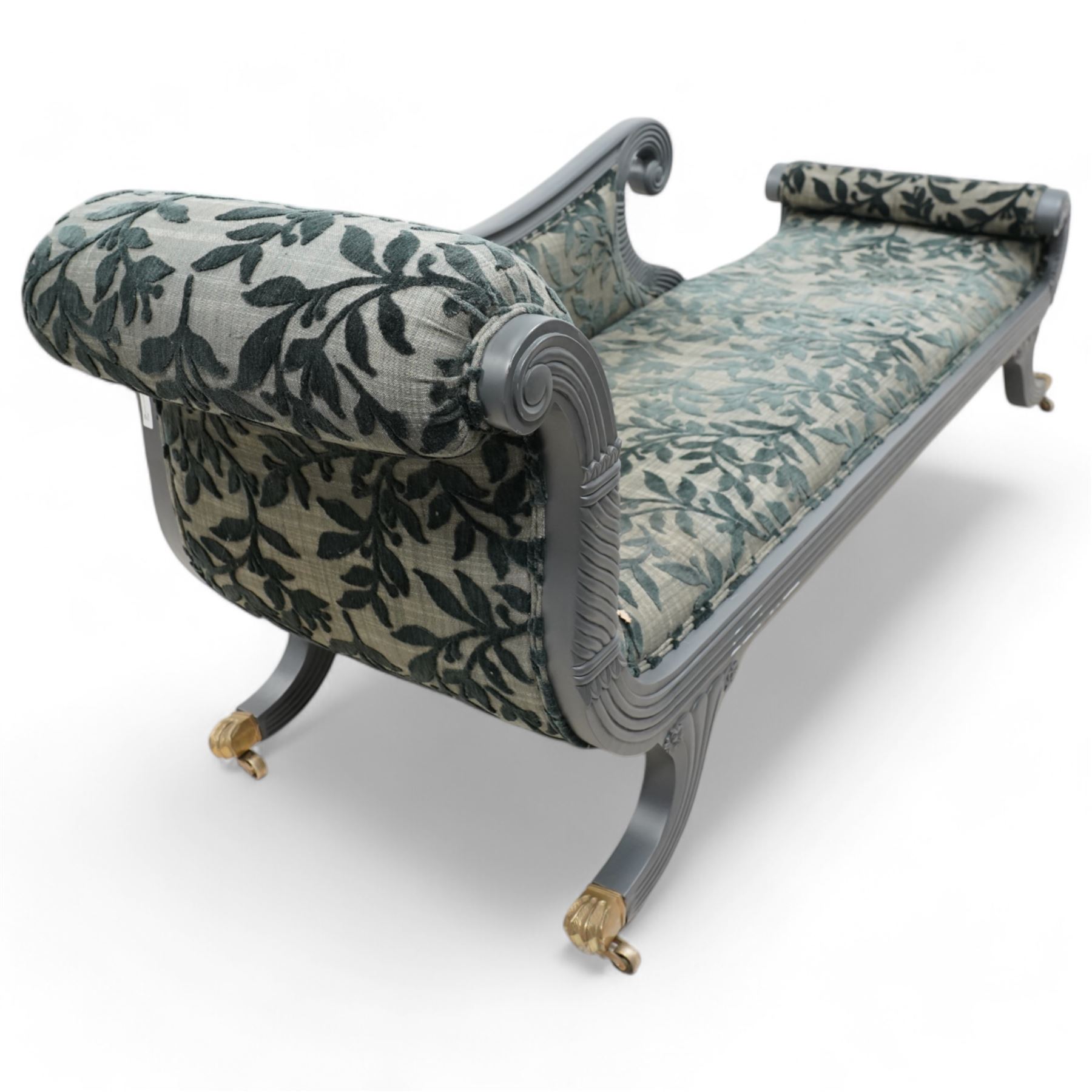Regency design hardwood-framed chaise longue, scrolled back upholstered in leafy branch pattern fabric, reeded and scroll carved frame, on out splayed feet with brass paw castors