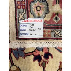 Northwestern Persian Heriz hand-knotted rug,  ivory field with a bold stepped medallion in madder red, navy and pale blue, surrounded by angular floral motifs and stylized leaves, the spandrels in camel and rose with a madder-red border of rosettes and angular vine motifs between multiple guard stripes, 180cm x 156cm