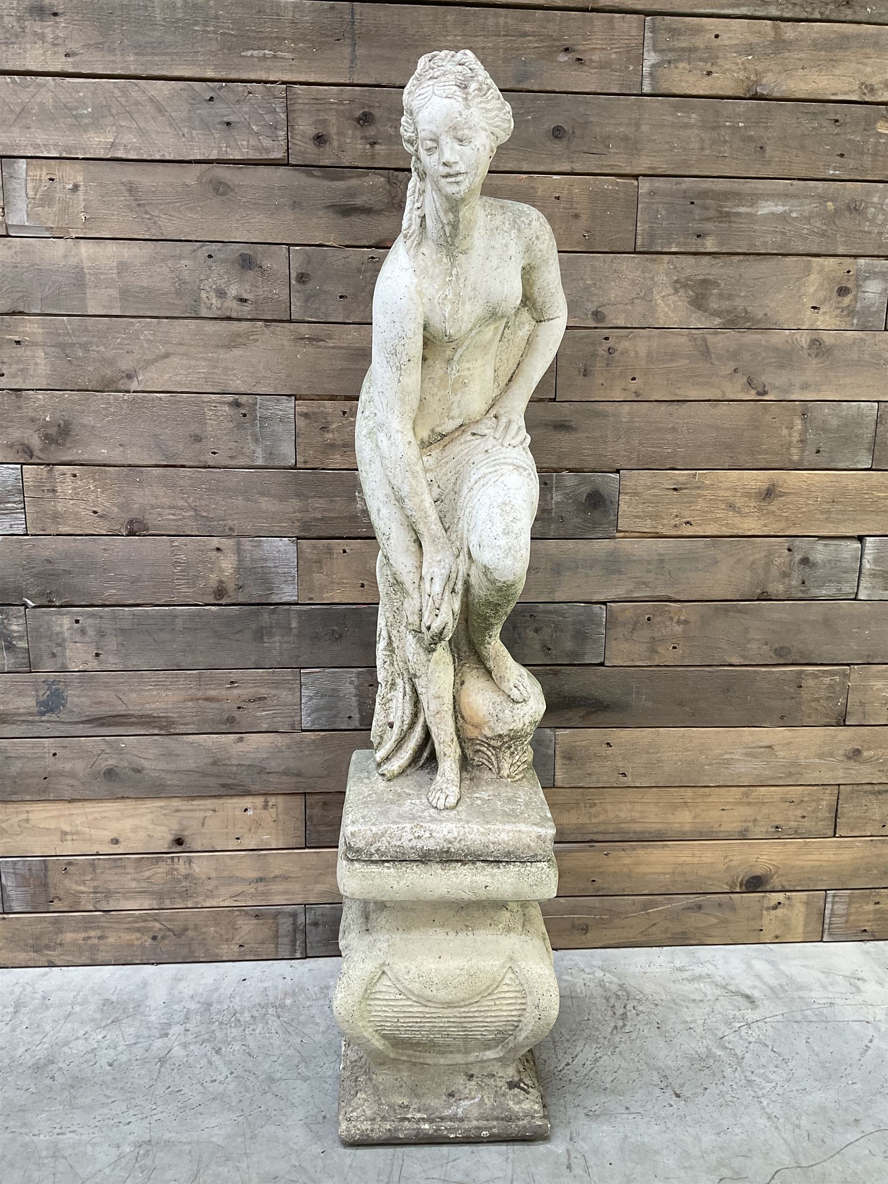 Cast stone garden statue of partially draped classical female figure on ornate pedestal 