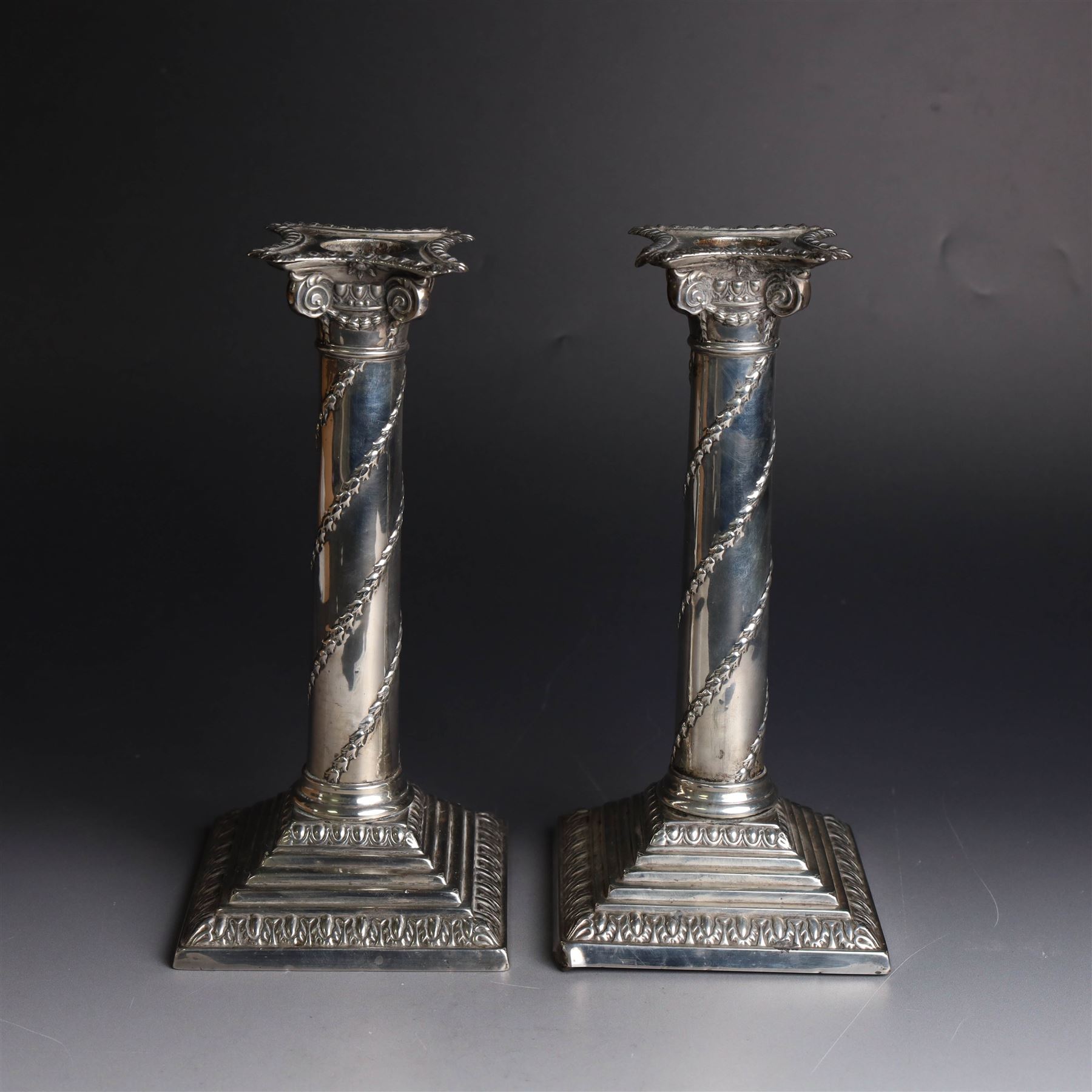 Pair of Edwardian silver mounted column candlesticks, each with embossed floral, foliate and scrolling decoration and upon stepped square weighted bases, hallmarked William Hutton & Sons Ltd, London 1901, H19cm