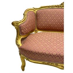 20th century French design hardwood framed giltwood settee, moulded cresting rail carved with central shell motif and extending scrolled foliage, upholstered in pink fabric decorated with repeating pattern, on cabriole supports with scroll carved terminals 