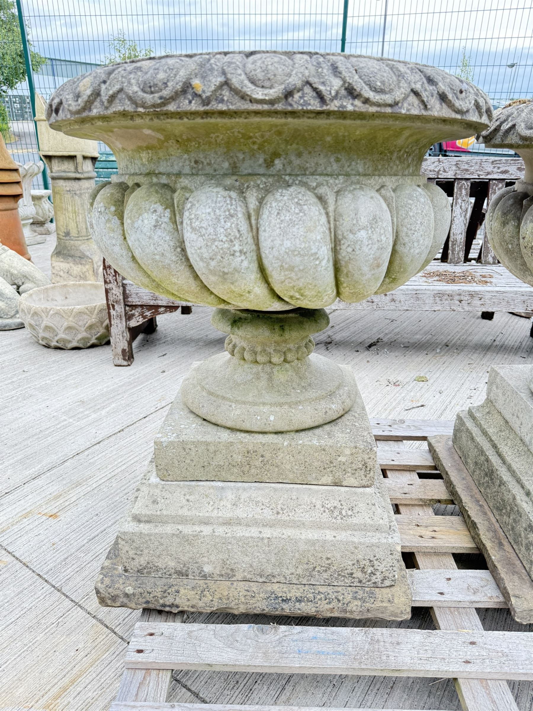 Pair of large weathered Country House Haddonstone garden urns, acanthus carved rim above gadrooned bowl, beaded detailing to the neck, raised on stepped double plinth base
