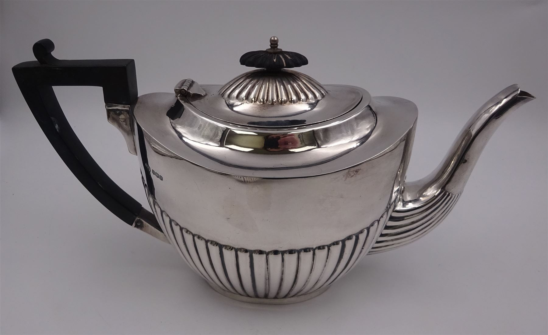 Early 20th century silver three piece tea service, comprising teapot, twin handled sucrier, and milk jug, each of oval part fluted form, the teapot with ebonised handle and finial, hallmarked Sheffield 1918, maker's mark WHM