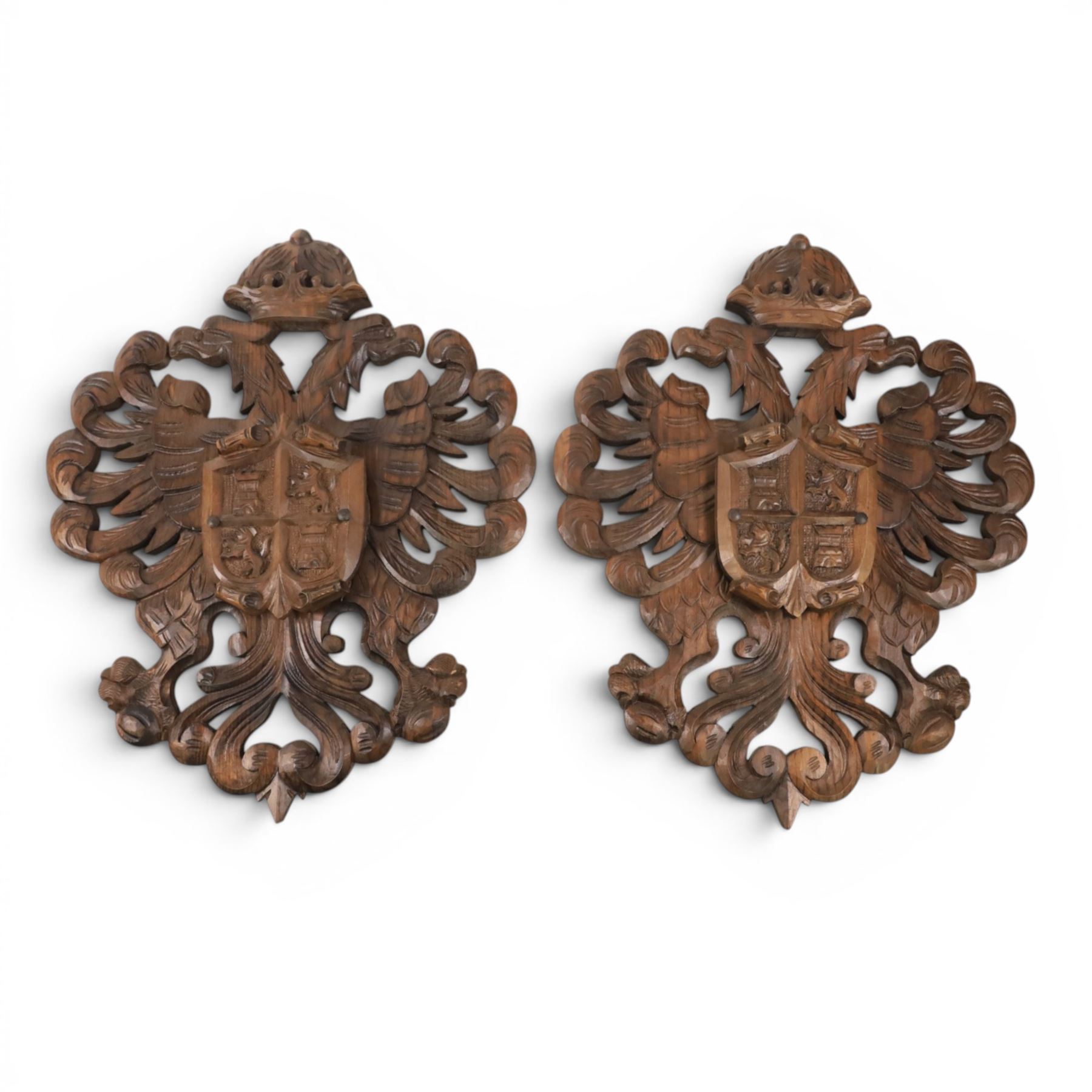 Carved wooden wall plaque, decorated with foliate scrolls, with two reproduction swords attached, together with five other wooden plaques with foliate scrolls and shields
