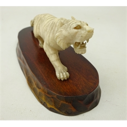  Early 20th century Japanese carved ivory bridge of nine graduating elephants on carved hardwood stand, L40cm and a Meiji period Japanese Okimono carved as a prowling tiger on hardwood base, L13.5cm and three other pre 1947 Indian carved ivory models (5)  