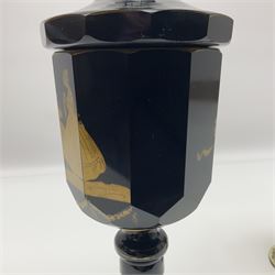 19th Century Bohemian amethyst glass lidded goblet, the bowl of faceted form, gilded with three children in period dress playing games, upon a knopped stem and conforming faceted foot, together with an art nouveau green glass goblet, with gilded rim, upon clear trumpet stem, and a hand blown wine glass, transfer printed with birds and three figures in period dress, tallest H29cm