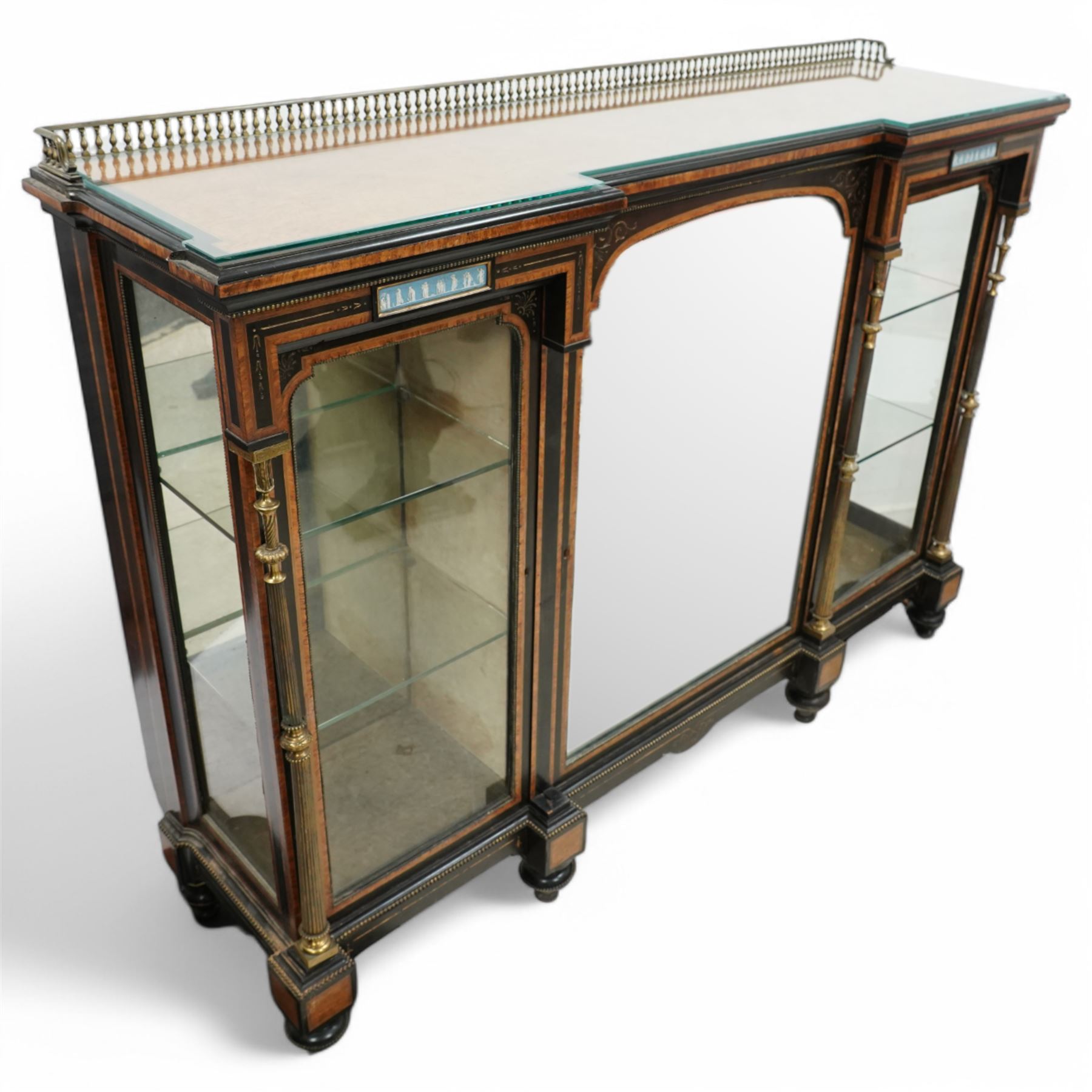 Victorian amboyna and ebonised credenza with glass top, the freeze fitted with two Wedgewood plaques and brass beading above crossbanded arched glazed mirror door flanked by two glazed cabinet doors with two removable glass shelves between four gilt brass reeded floral columns, supported on bun style feet
