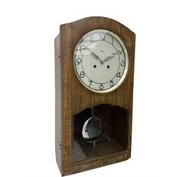 A mid 20th century German wall clock in a veneered mahogany case with a German eight day 'Kienzle' movement sounding the hours and half hours on twin gong rods, 9' circular dial with chrome Arabic numerals and pierced baton hands,  full length door with glazed dial and pendulum apertures, chrome pendulum bob. 
 


