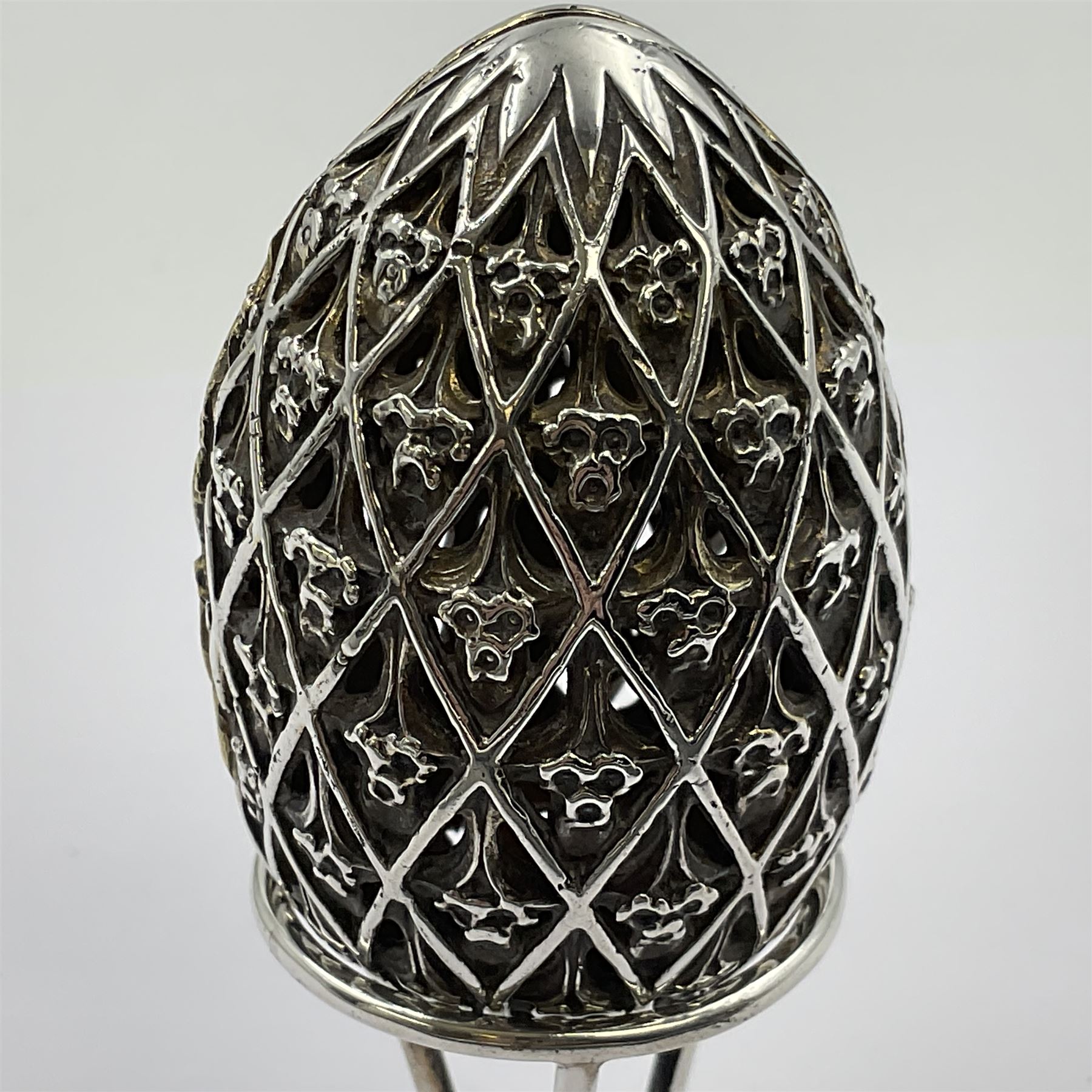 Modern silver limited edition Easter egg, no. 70/500, the openwork lattice body decorated with gilded panels of flower heads, opening to reveal a gilt interior, upon silver stand with three scrolling pad feet, each hallmarked St James House Company, London 1979, height including stand 8cm