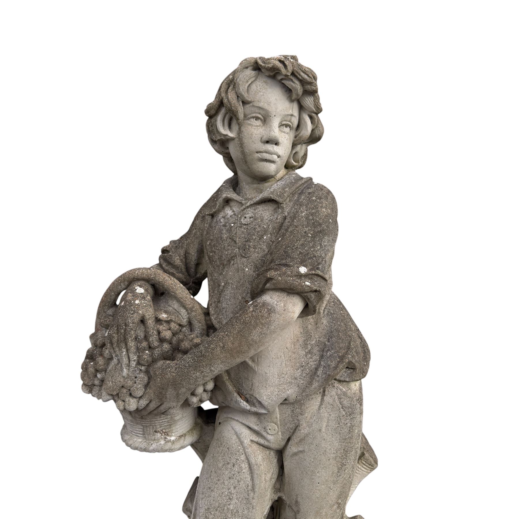 Haddonstone - weathered cast stone garden statue of a boy holding a basket of grapes, modelled with curled locks of hair wearing a tunic and breeches leaning against a naturalistic tree stump, on square base