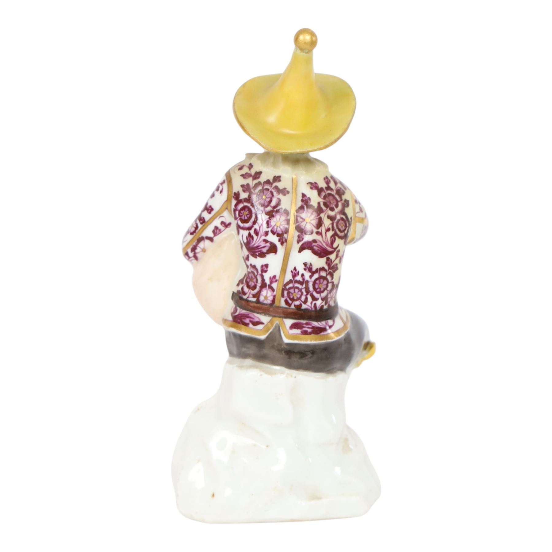 Mid 18th century Meissen figure, modelled as a harlequin playing bagpipes, circa 1745, possibly modelled by J.F.Eberlein after earlier models by J.J.Kändler, wearing a gilt edged tunic painted with flowers, black breeches with rosettes at the knees, red shoes and conical yellow hat, seated upon a rock, with traces of blue crossed swords mark beneath, H14cm