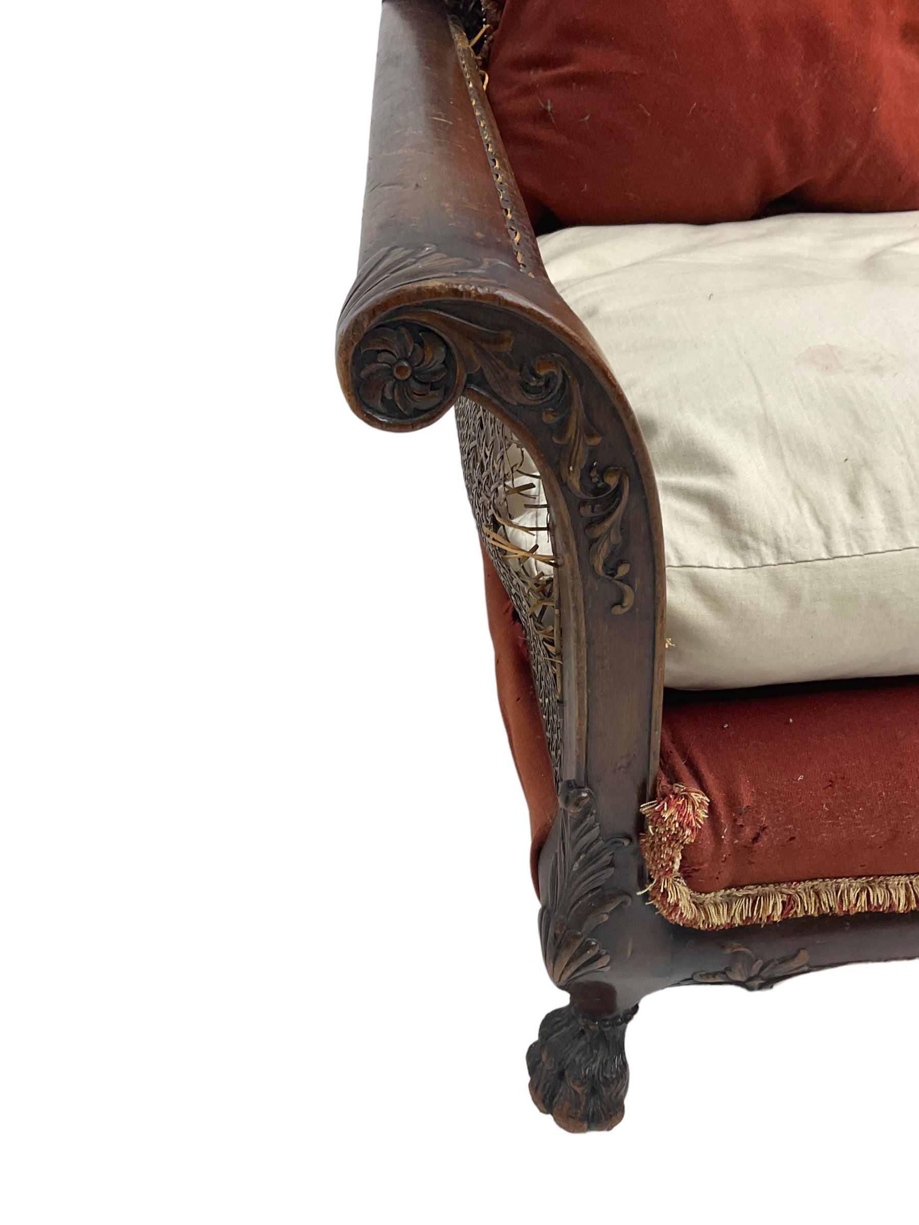 Early 20th century bergère three seat settee, shaped shell carved cresting rail, double caned back and sides, scrolled upright arms and shaped apron carved with shell and foliage, on hairy paw carved feet