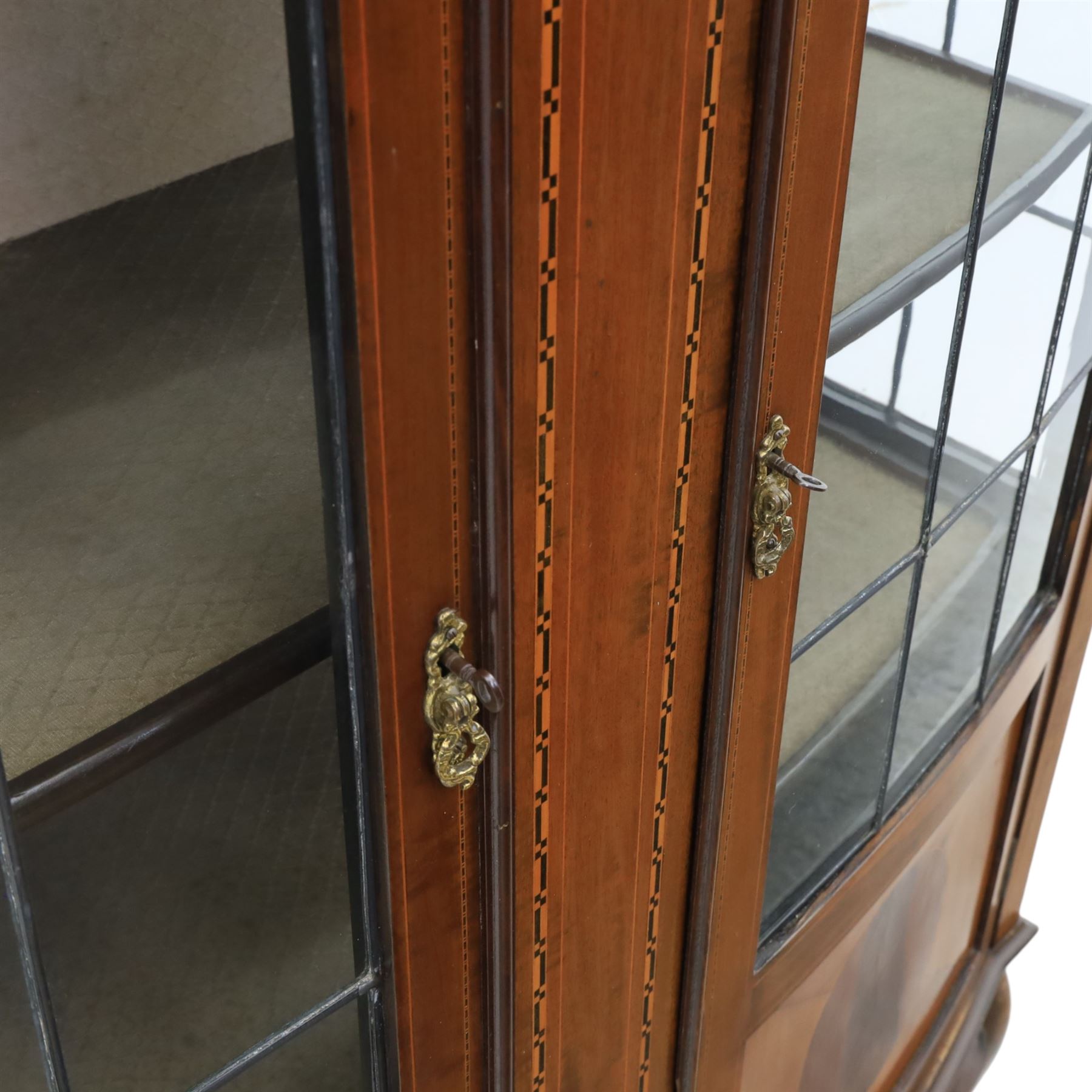 Edwardian mahogany display cabinet, arched back with satinwood and harewood marquetry foliate decoration above a moulded cornice, serpentine front fitted with twin glazed doors with astragal bars, the lower door panels inlaid with oval reserves, standing on elegant cabriole legs terminating in pad feet