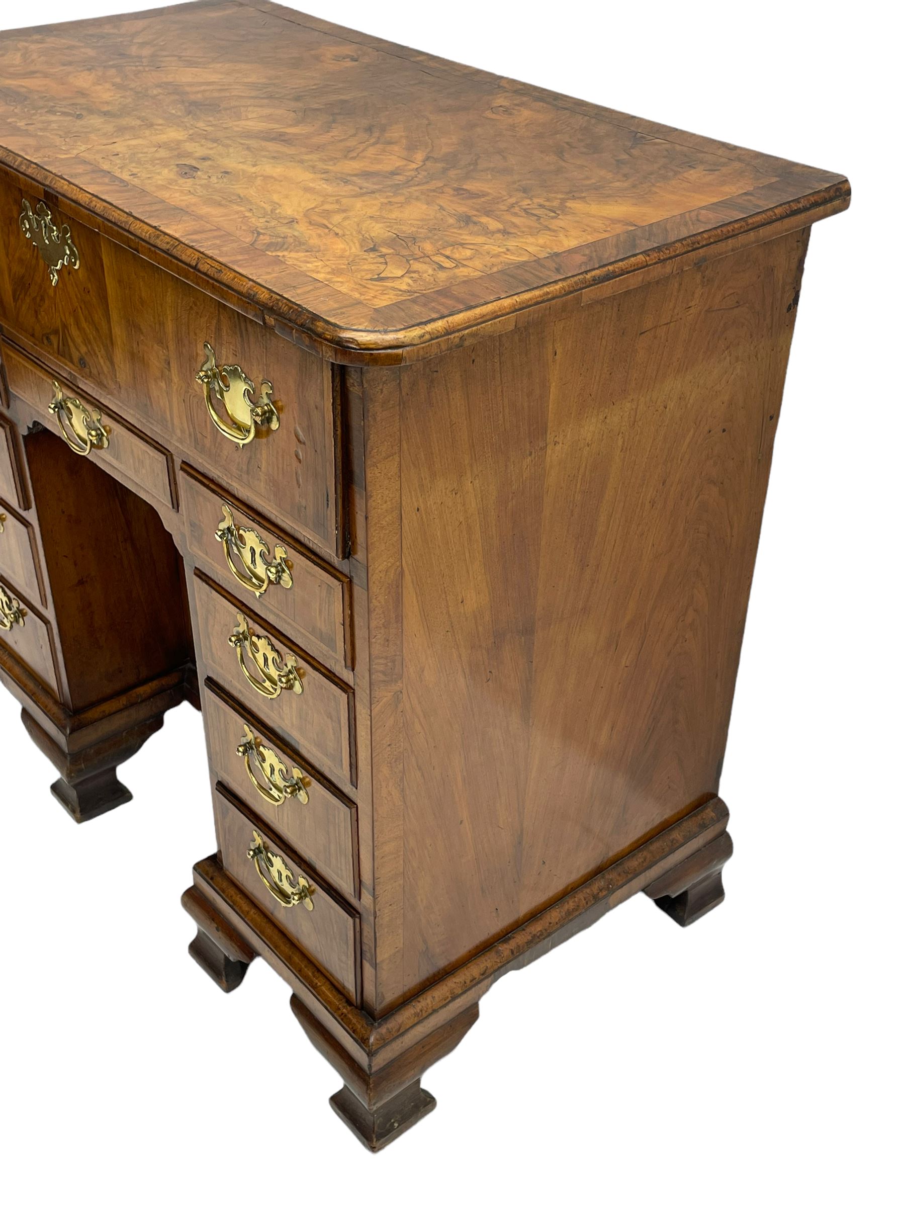 Early 18th century Queen Anne figured walnut kneehole desk with secretaire drawer, moulded and book matched top with walnut band, the top drawer with fall front enclosing small drawers and pigeon holes, fitted with nine drawers and central recessed cupboard, on ogee bracket feet