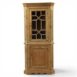 19th century stripped pine corner cabinet, projecting cornice flanked by fluted sides, astragal glazed upper door with brass knob, lower section with fielded panelled door, raised on a shaped plinth base 