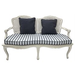 French design white painted two seat serpentine settee, floral carved cresting rail over cane back, loose striped upholstered seat cushion, on cabriole supports