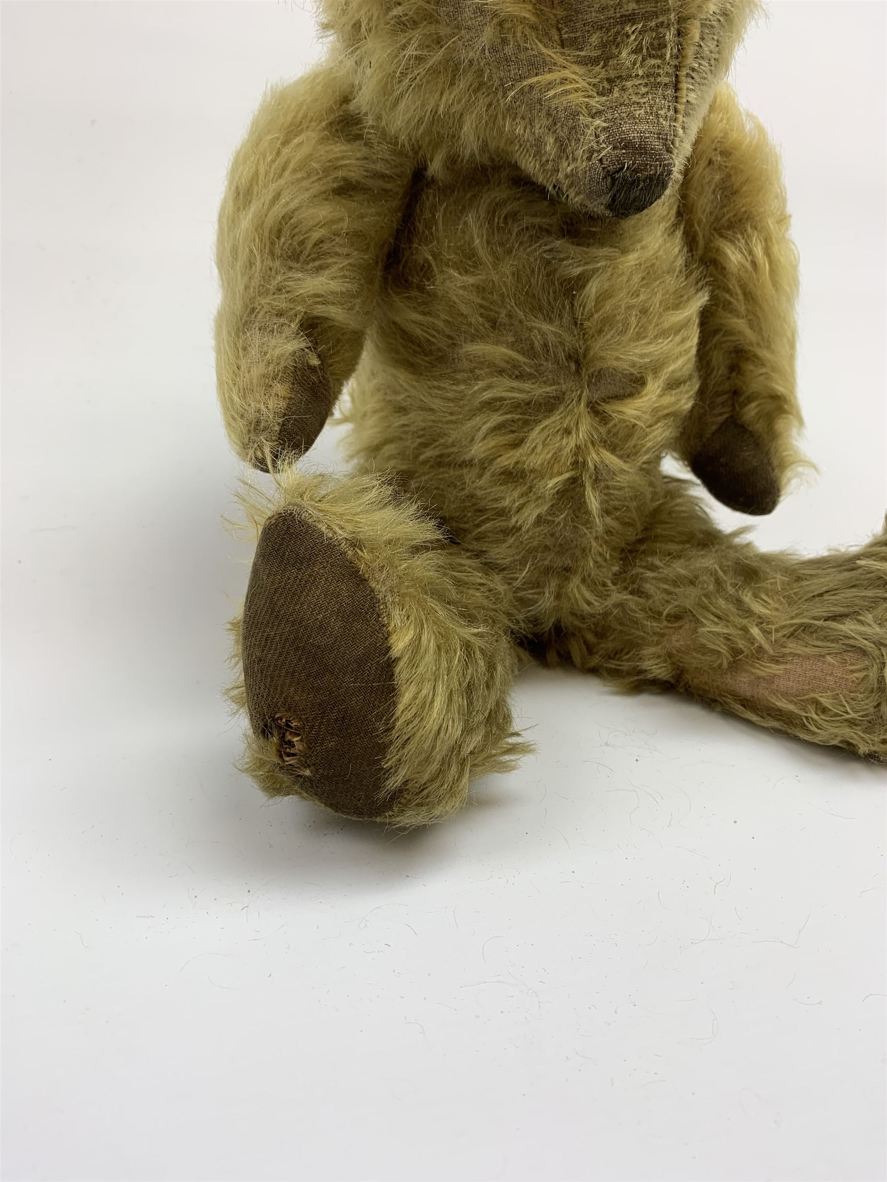 Early 20th century English teddy bear, WW1 period, with wood wool filled mohair body, fixed head with one boot button eye and vertically stitched nose and mouth and jointed limbs with cloth paw pads H16