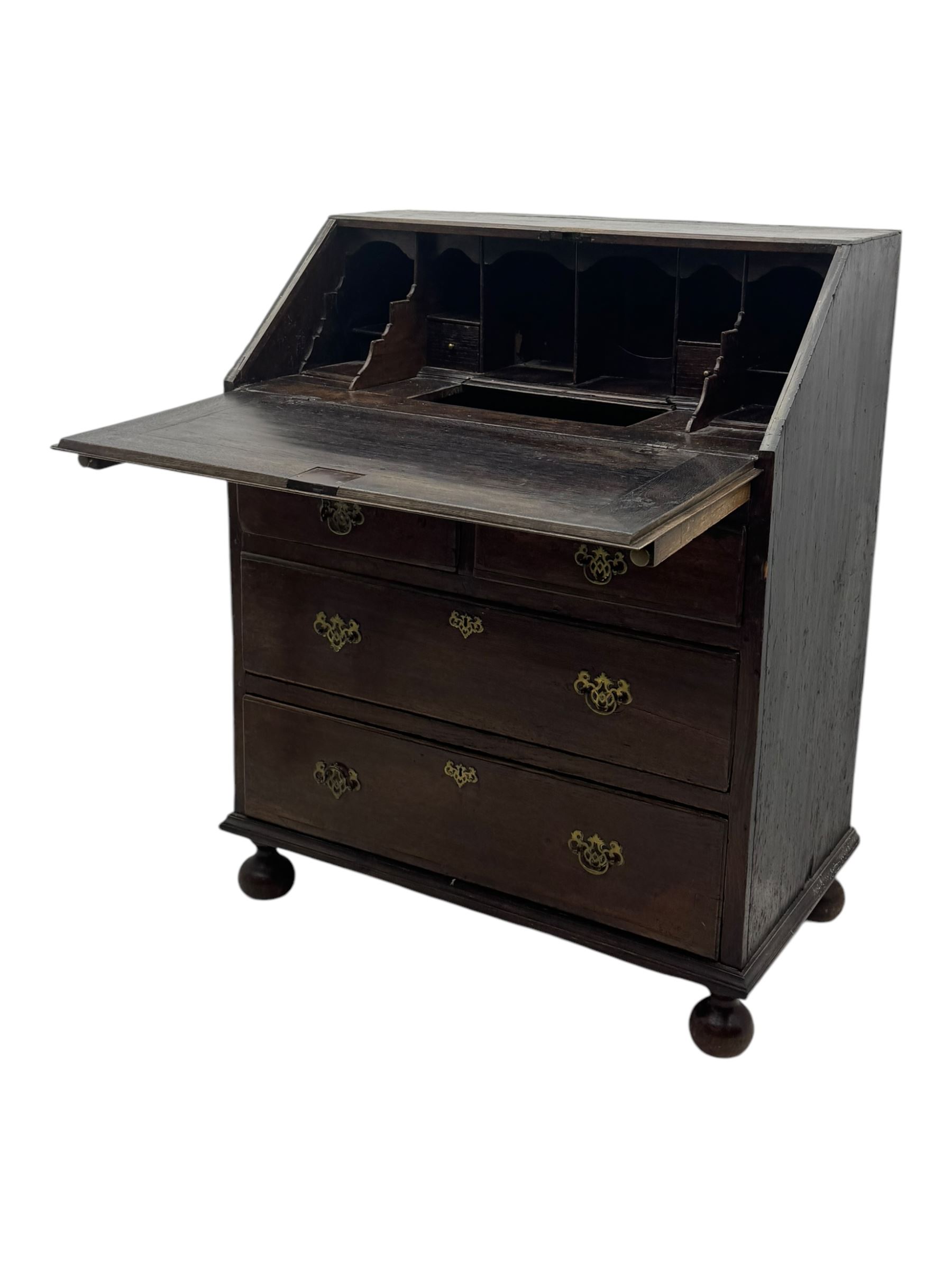 George III oak bureau, sloped fall-front enclosing a fitted interior with pigeonholes, small drawers, and a central compartment, over two short and two long drawers, brass escutcheons and drop handles, raised on bun feet