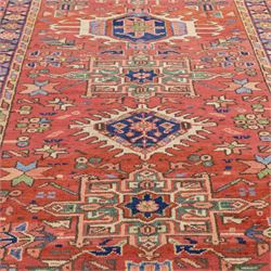 North West Persian Karajeh hand-knotted runner, madder red field, decorated with a vertical sequence of bold geometric medallions, interspersed with stylized floral and tribal motifs, framed by a dark ground border of angular palmettes and rosettes with multiple guard stripes, with cotton fringe ends 