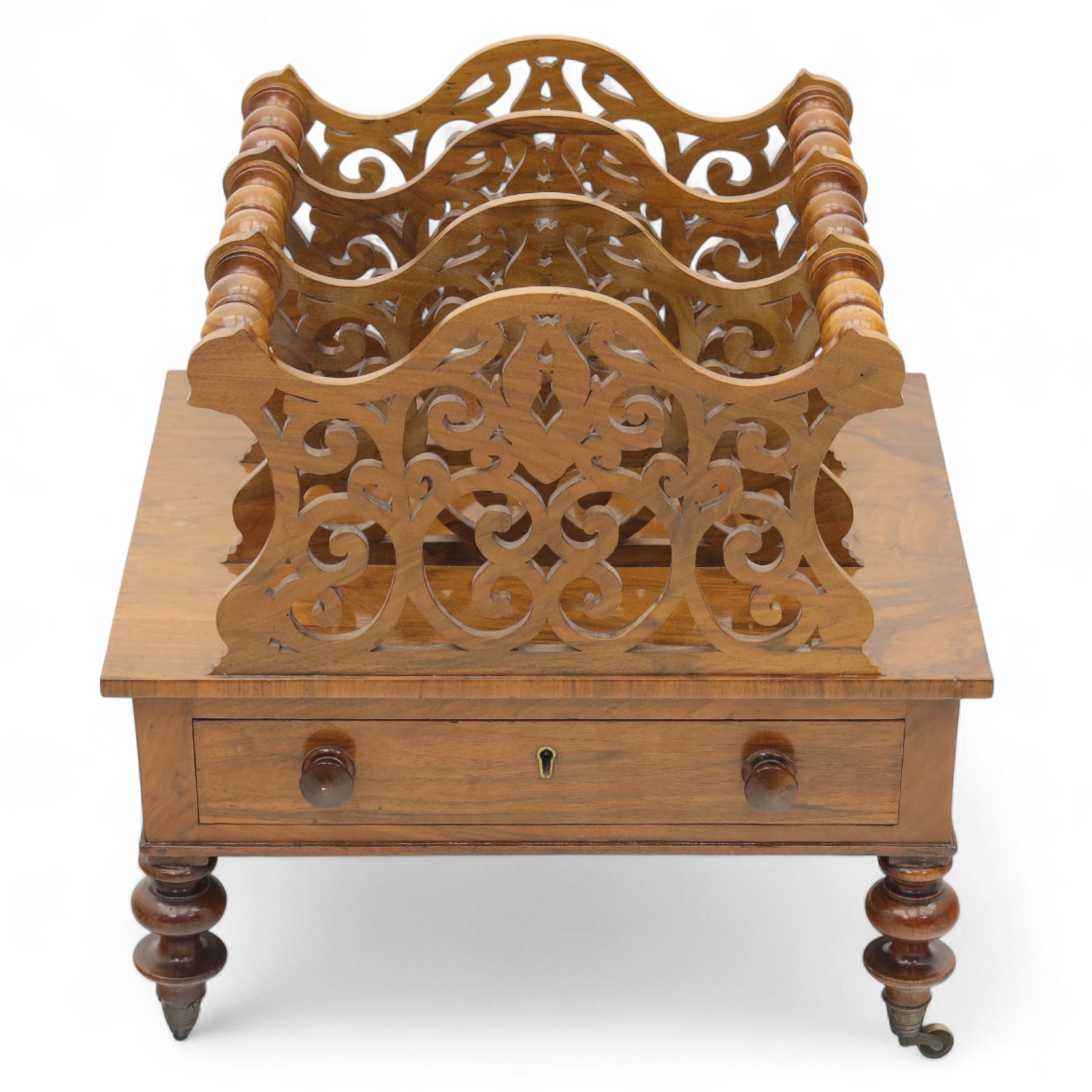 Victorian walnut Canterbury, scroll pierced divisions with turned carrying handles above a frieze drawer with knob handles, raised on turned legs terminating in brass castors