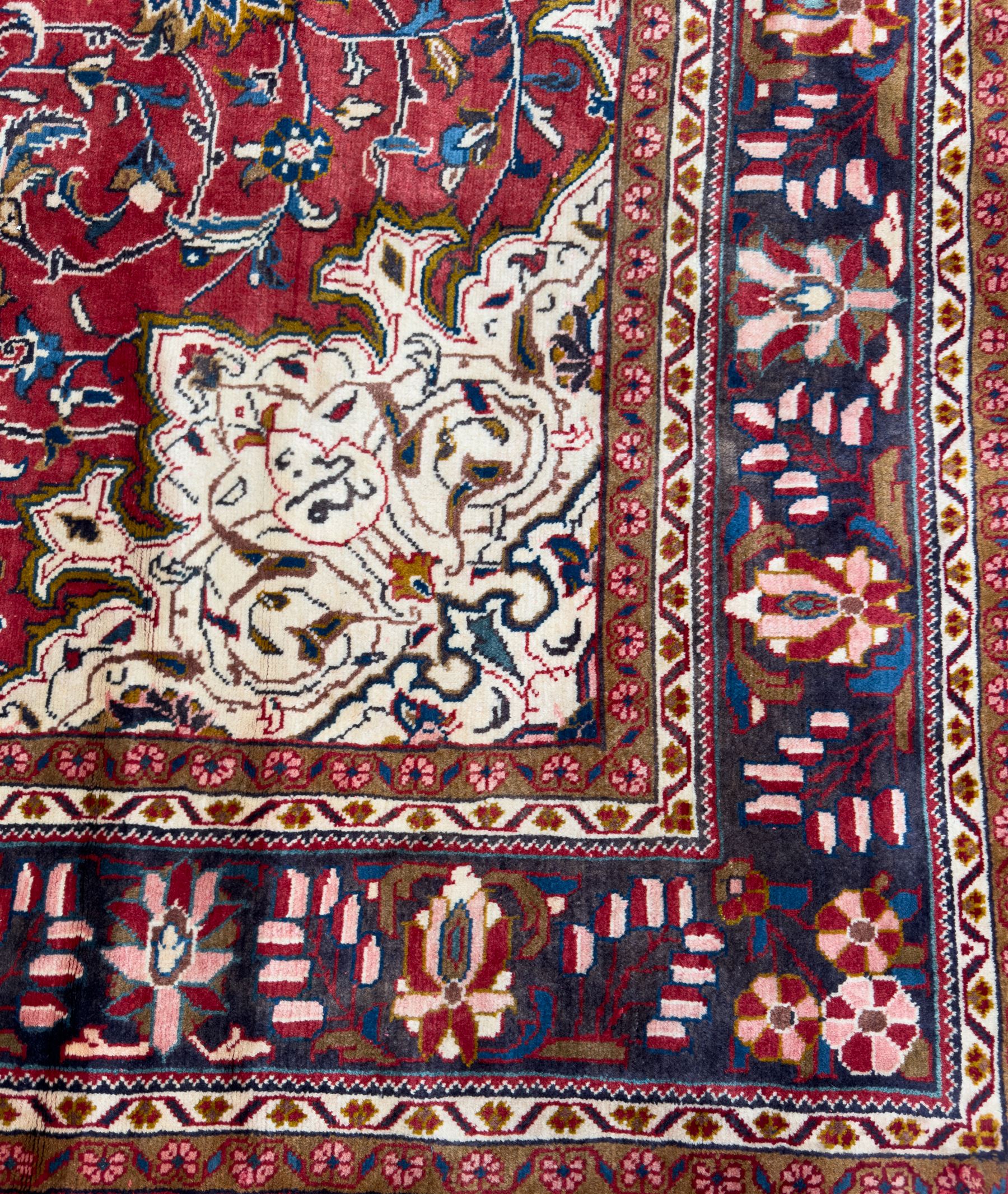Northwestern Persian Lillihan hand-knotted carpet, madder red field with scrolling vines, rosettes, and palmettes around a central circular medallion in navy, ivory and ochre, and ivory ground spandrels within a navy border of stylized flowerheads and vines between multiple guard stripes 