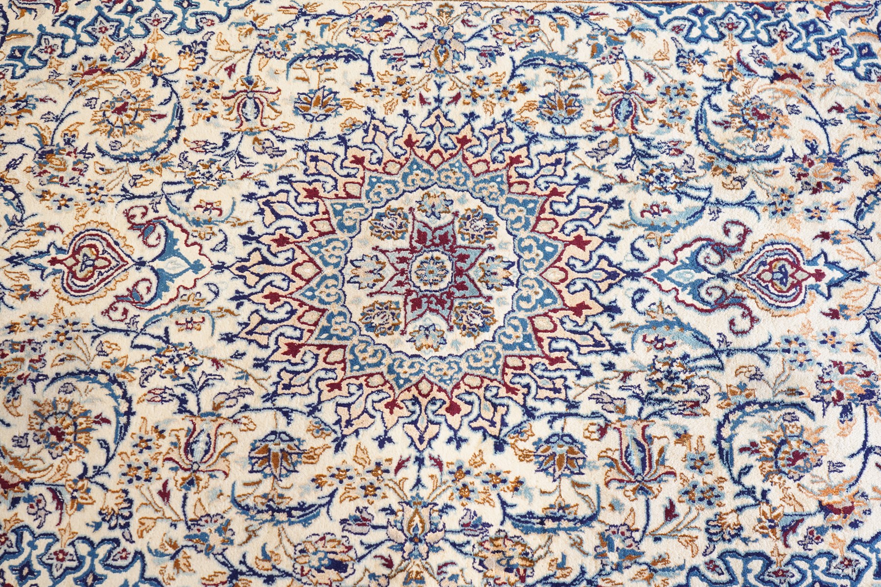 Persian Nain ivory ground rug, the busy oval field profusely decorated with scrolling foliate decoration and palmettes in citrine and indigo tones, the central medallion with matching spandrels, the multiple guard bands with repeating stylised quatrefoil motifs and trailing scrolling foliage and flowerheads